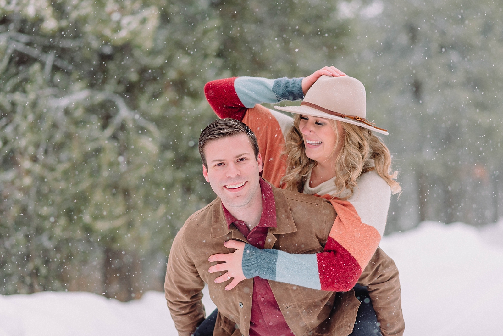 woman on man's back during outdoor engagement session wearing hat and striped sweater