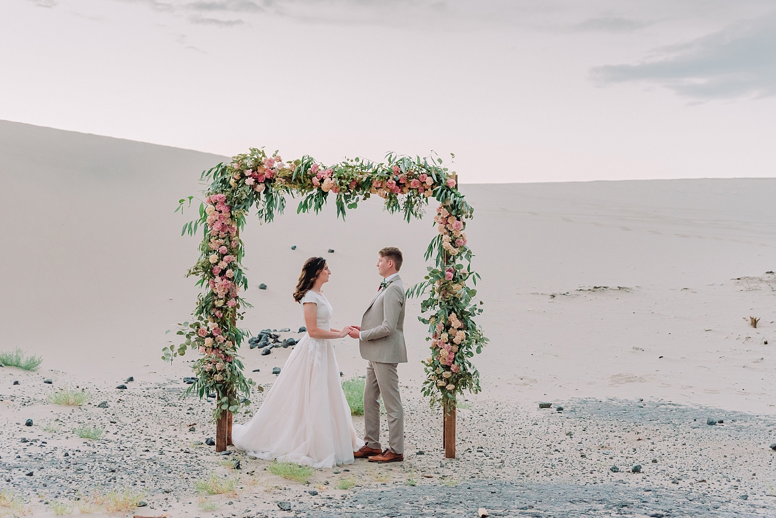 floral wedding arch in the desert with bride and groom holding hands while standing under the arch