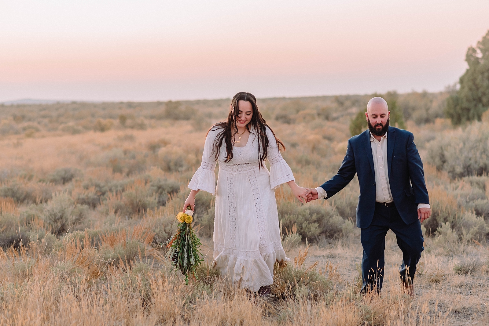 bride and groom holding hands walking through field of grass during fall elopement at hells half acre