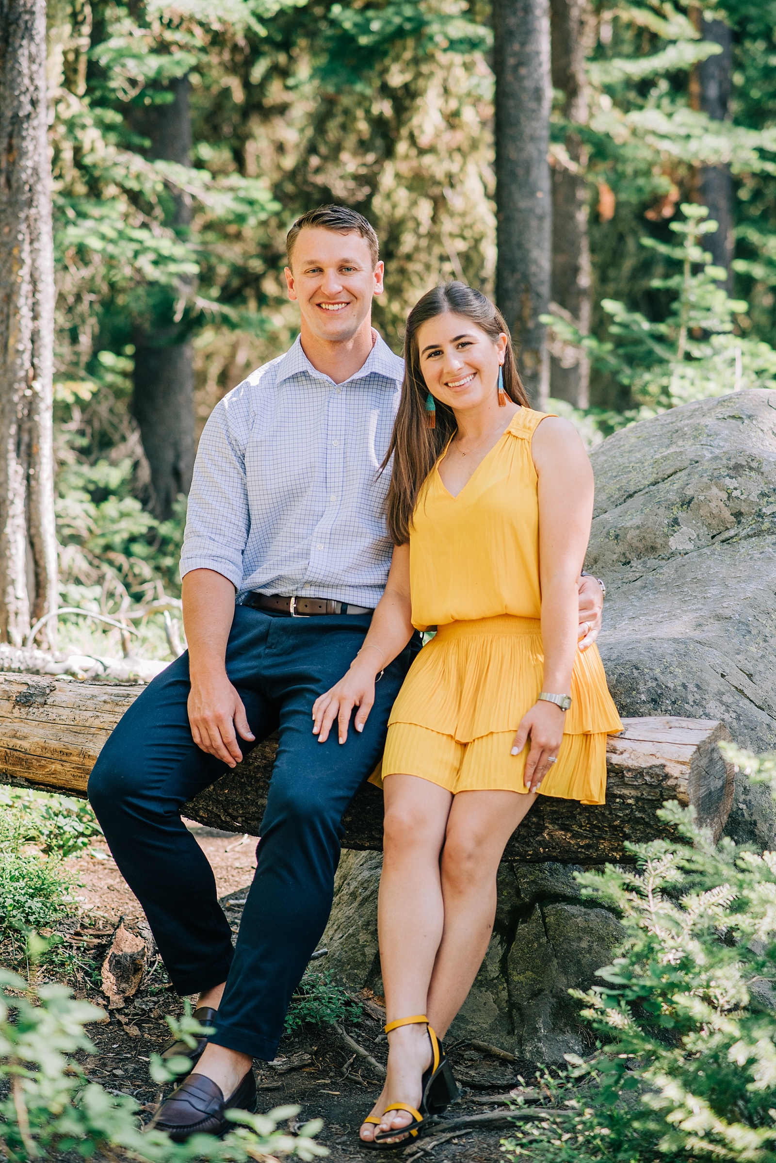 man and woman sitting on a fallen tree for their Jackson Hole honeymoon portraits with woman in a yellow sun dress
