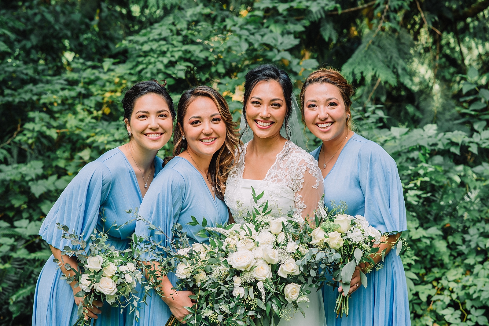 bride standing with her bridesmaids who are wearing blue gowns as they all hold their white bridal bouquets