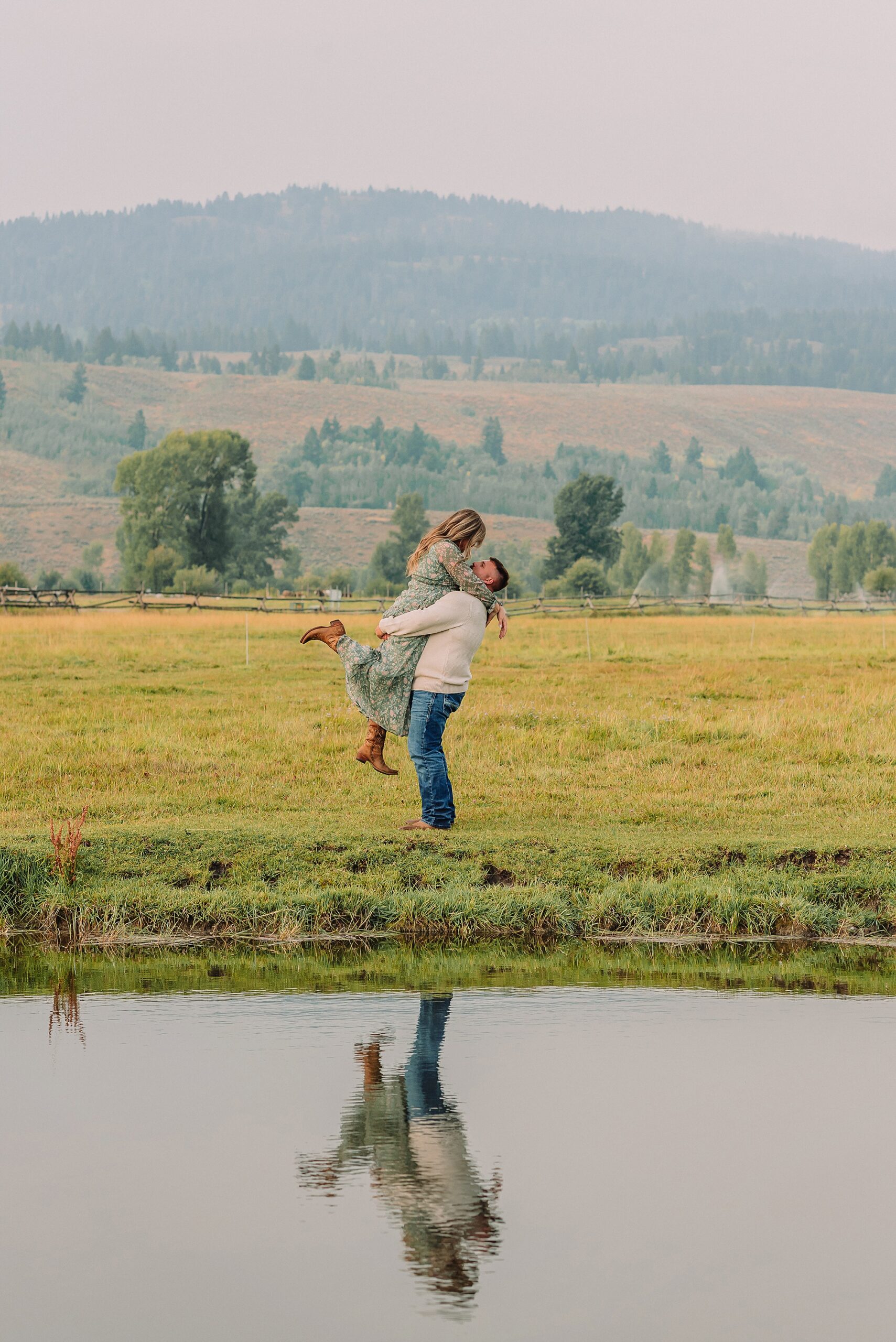 engaged couple poses with a lift pose where he is picking her up next to a pond