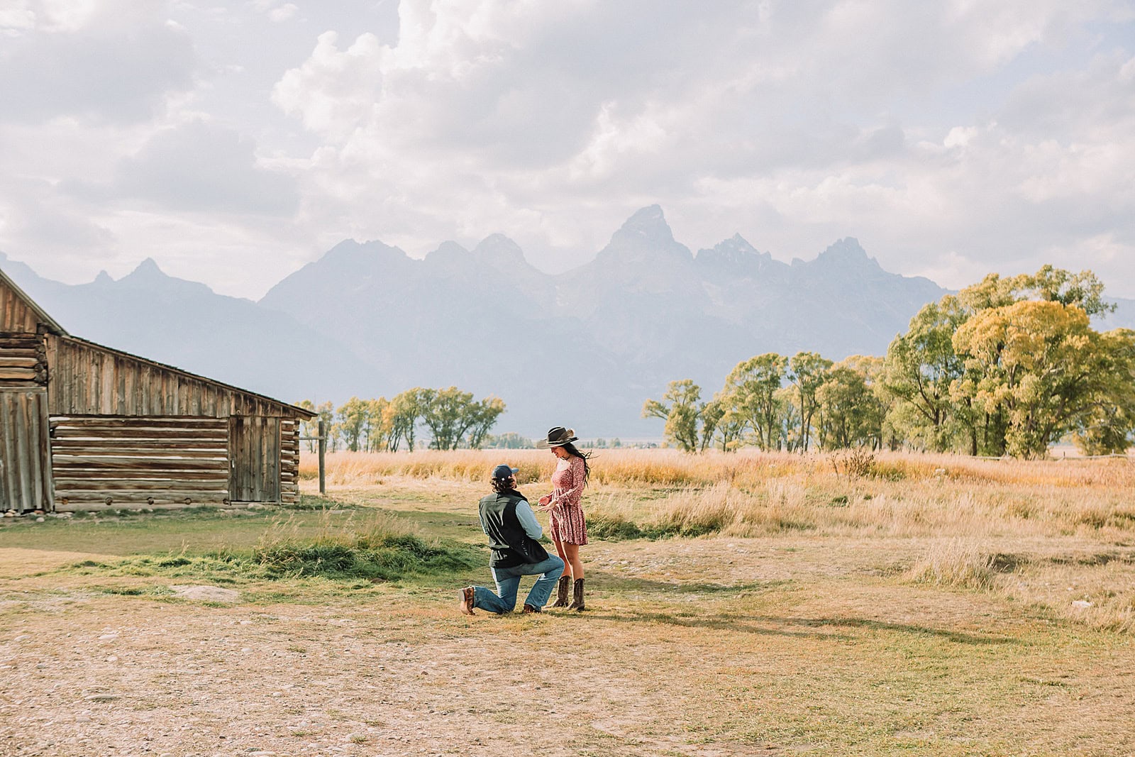 man proposes to girlfriend in fall mormon row proposal with golden grasses and the Teton Mountains