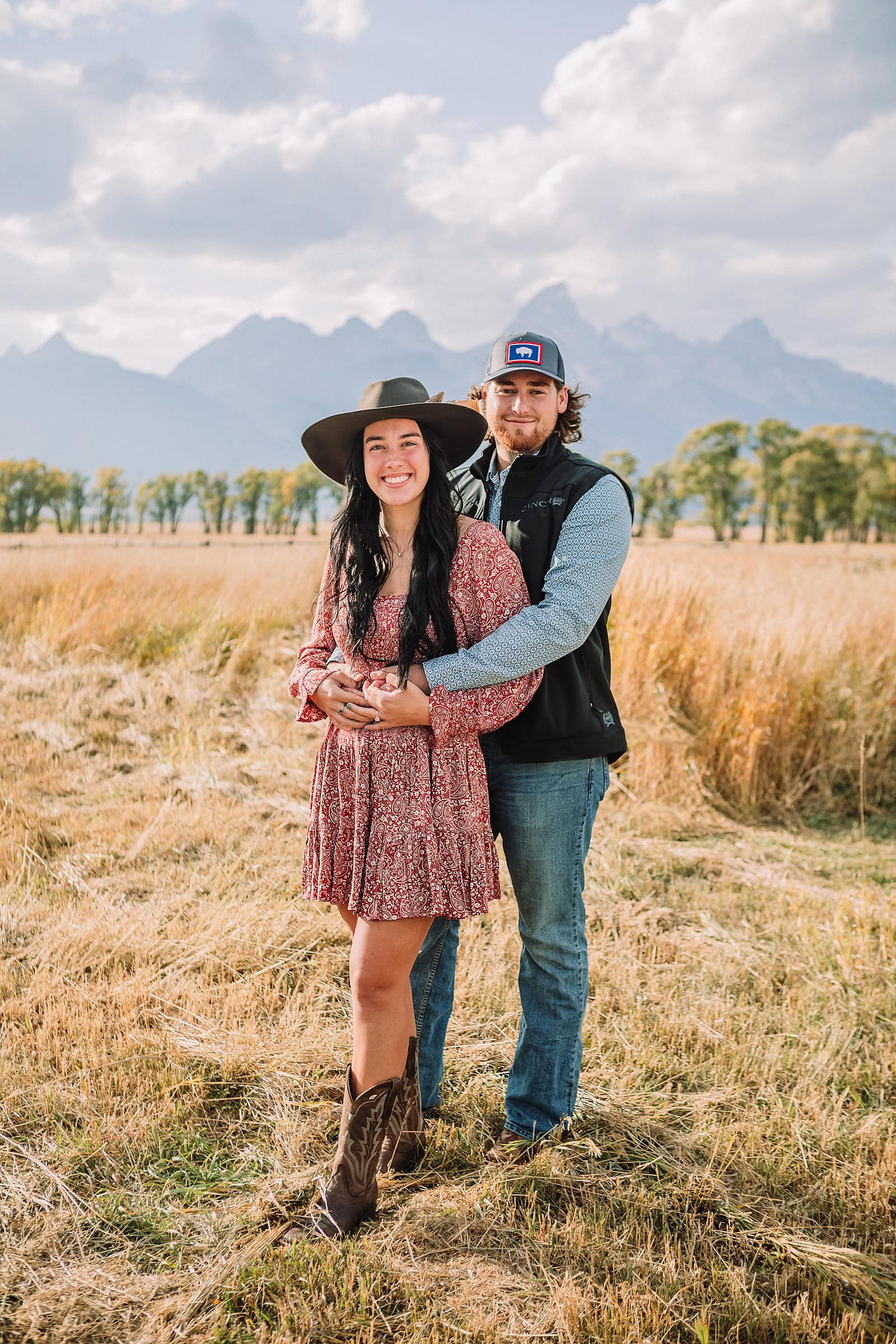 newly engaged couple pose in golden field with the Teton mountain range in the background