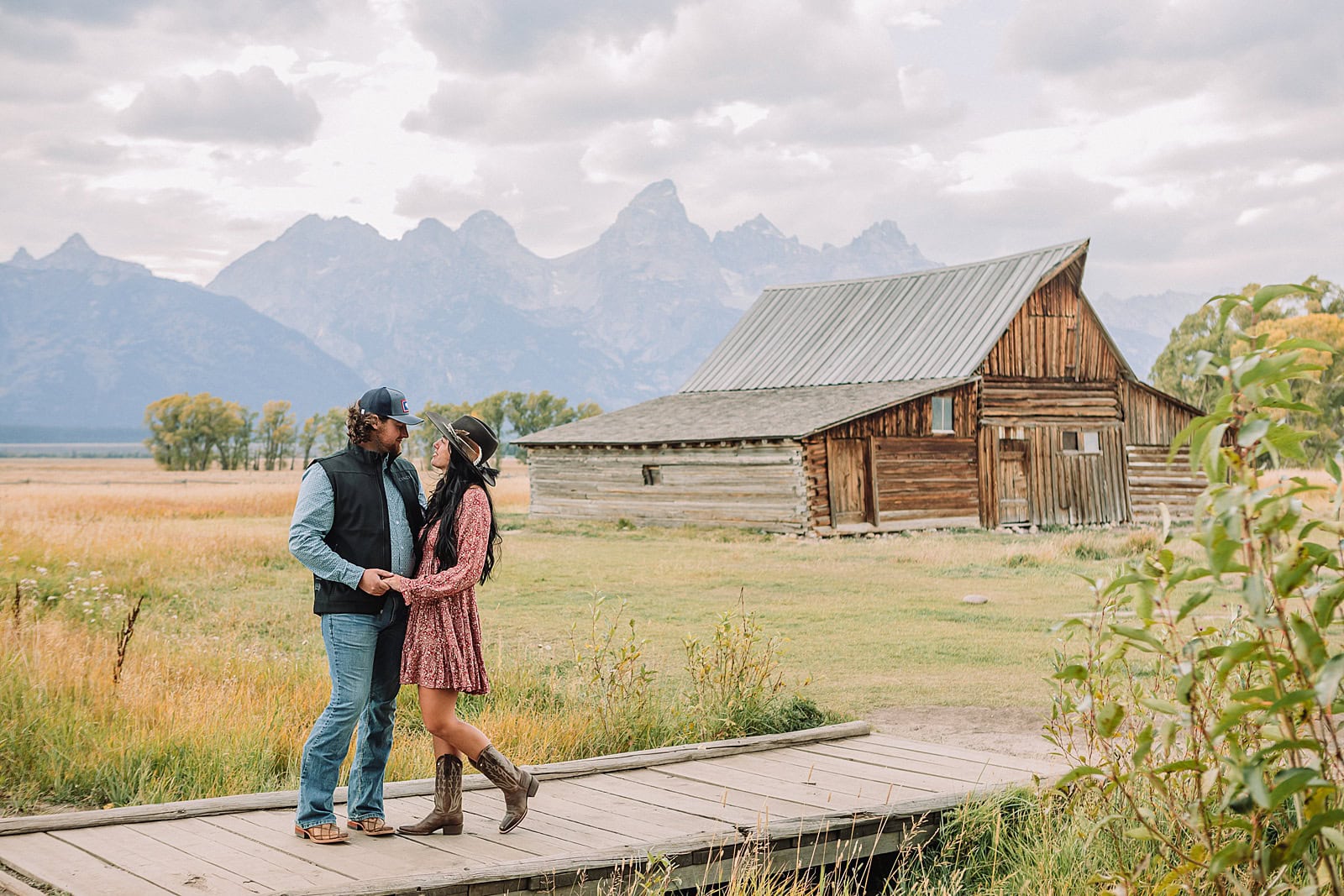 Engaged couple poses in front of the Teton Mountains and Moulton Barn