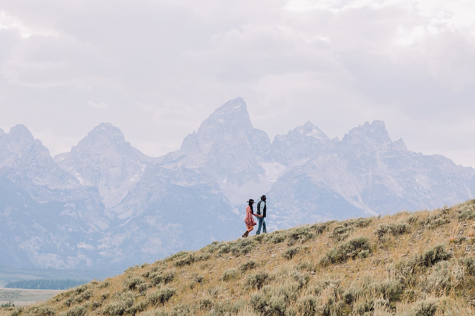 newly engaged couple pose in golden field with the Teton mountain range in the background