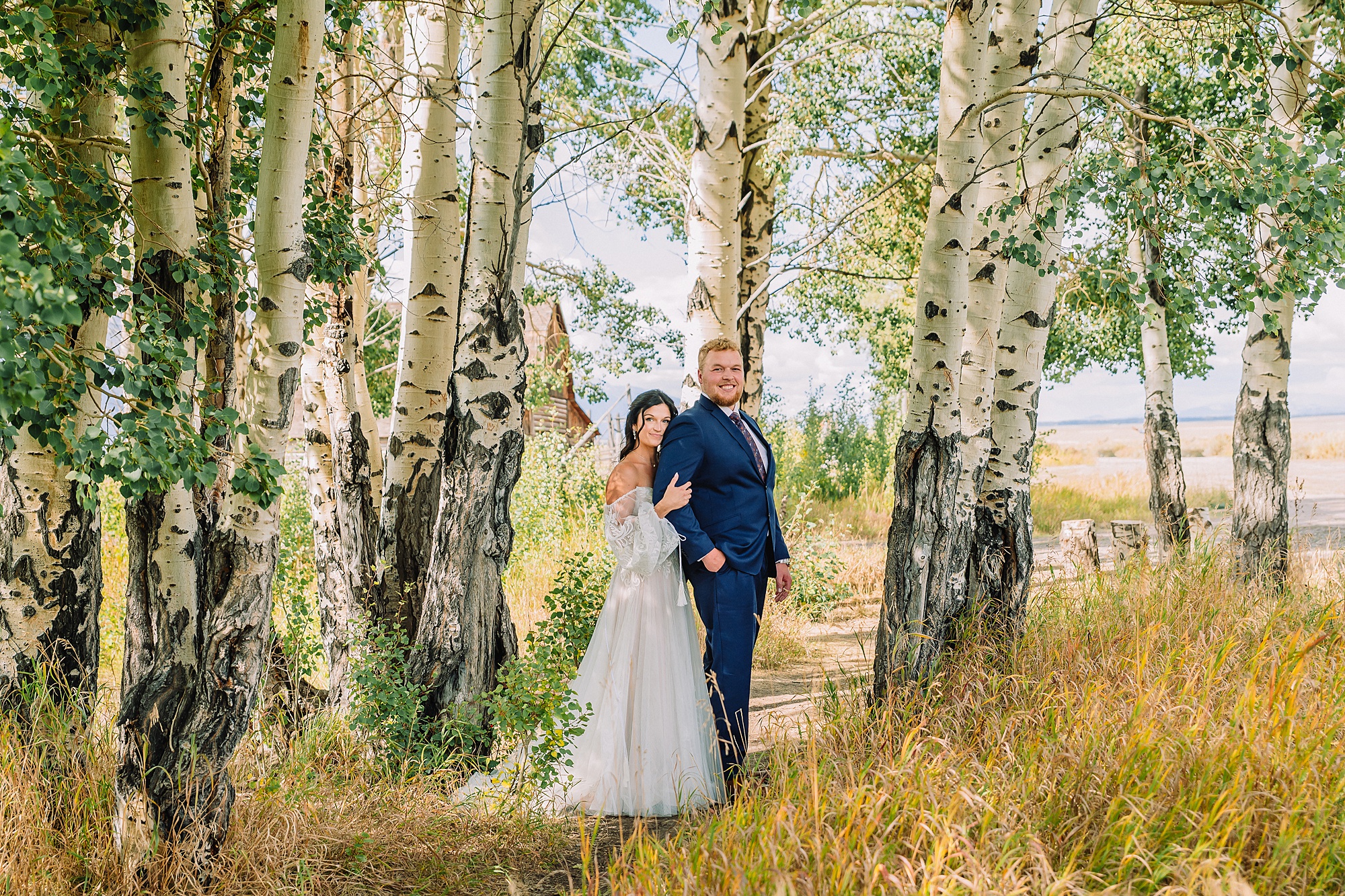 bride and groom in wedding attire stand in a copse of aspen trees