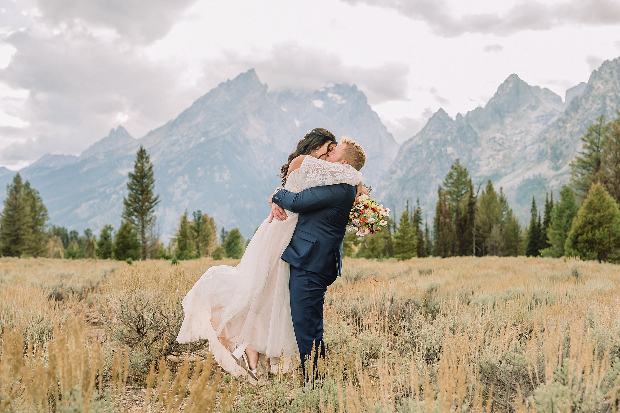 groom lifts bride in a lifting pose and kisses her in the Tetons