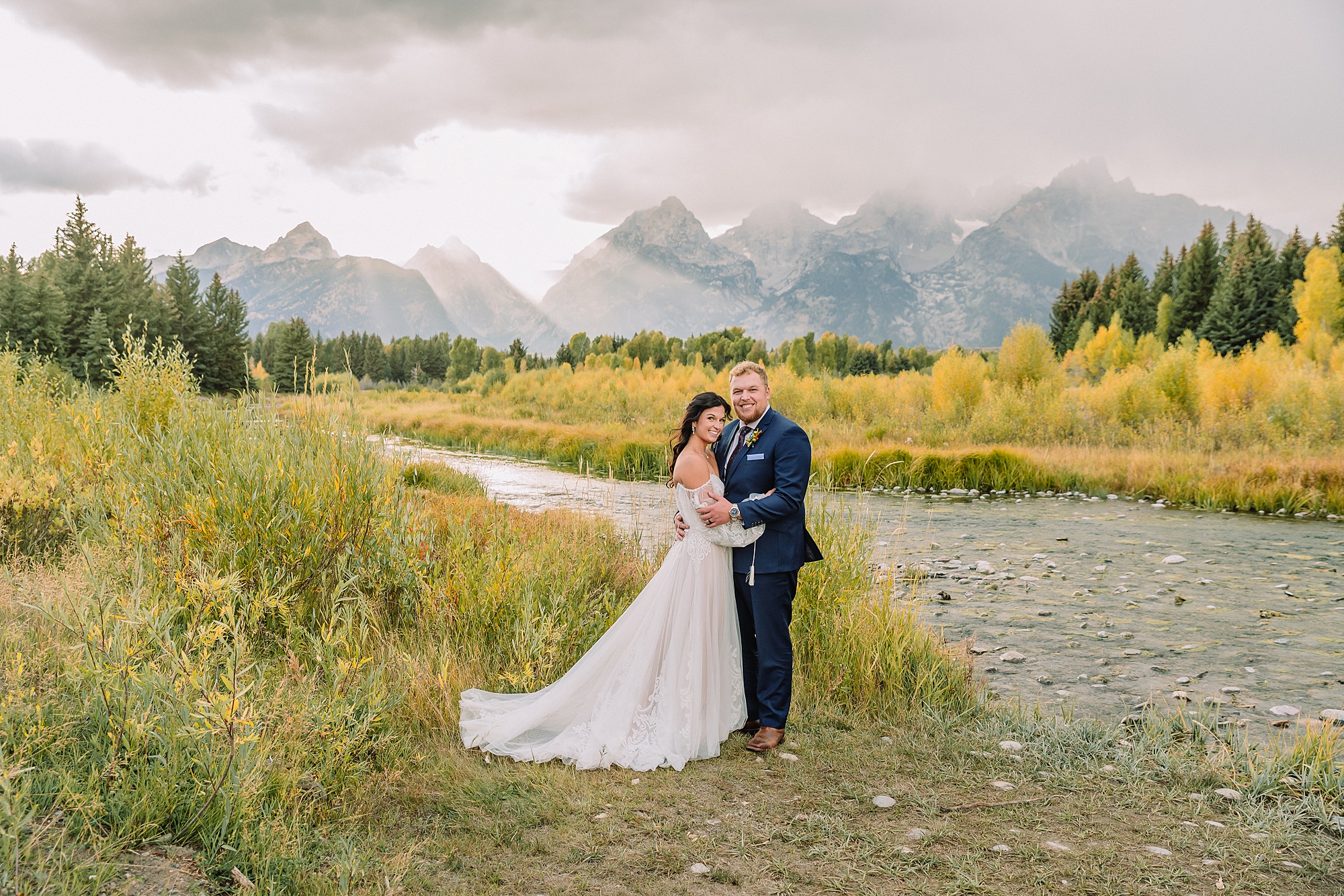 wedding couple at schwabacher landing in flowy dress and blue suit, with god rays behind them