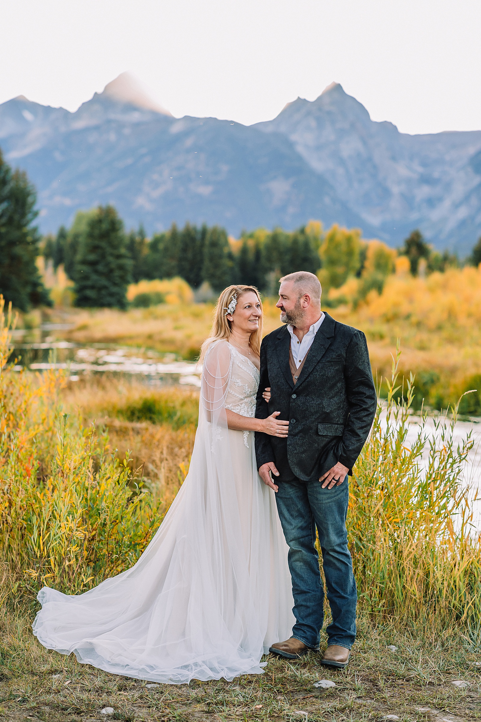 Jackson Hole honeymoon wedding photos Schwabacher Landing wedding portraits Snake River wedding photography September mountain wedding photos beaded wedding dress golden hour western groom style wedding photos Teton mountain wedding portraits sheer cape wedding dress photography