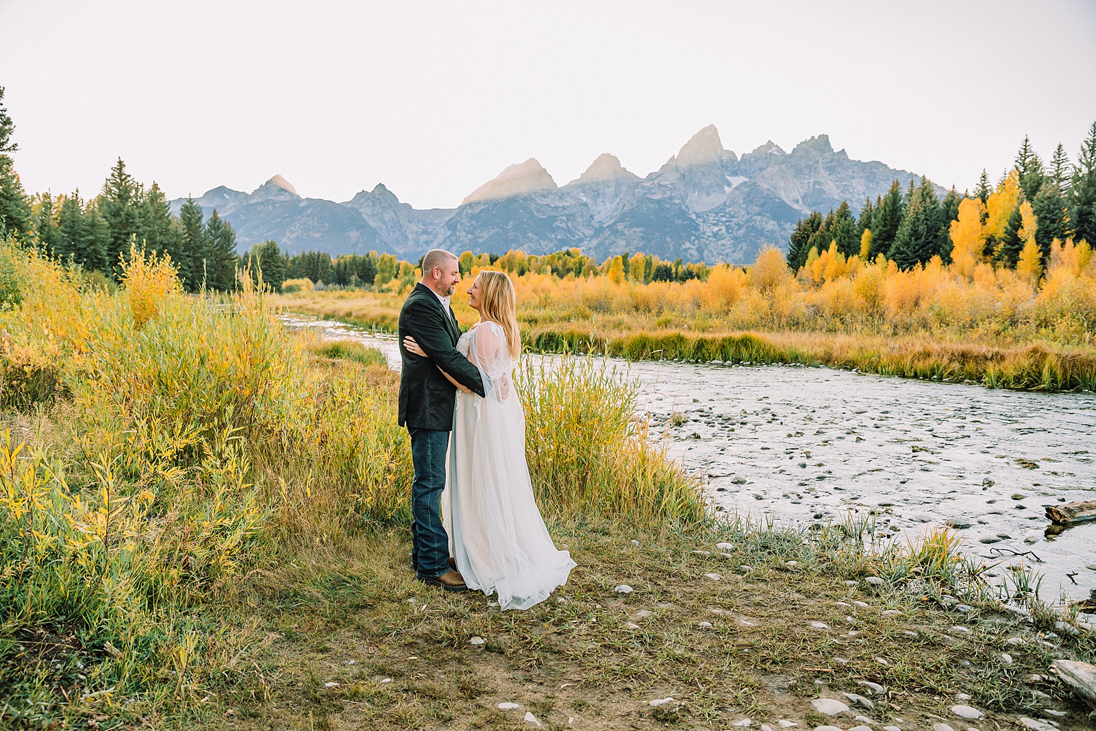 Jackson Hole honeymoon wedding photos Schwabacher Landing wedding portraits Snake River wedding photography September mountain wedding photos beaded wedding dress golden hour western groom style wedding photos Teton mountain wedding portraits sheer cape wedding dress photography