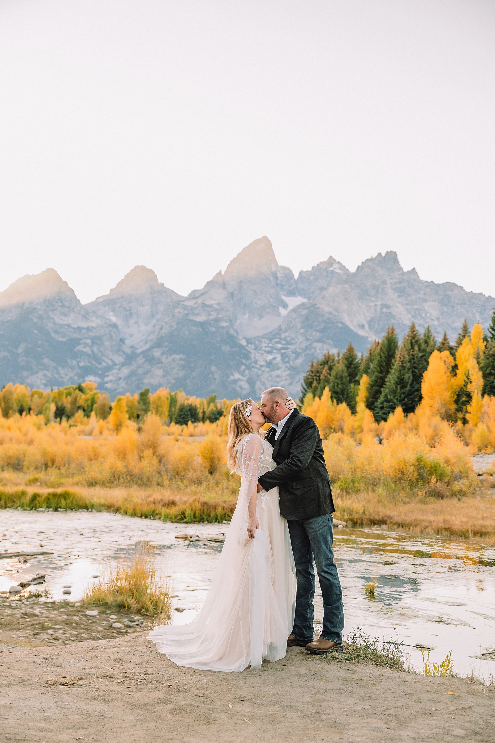 Jackson Hole honeymoon wedding photos Schwabacher Landing wedding portraits Snake River wedding photography September mountain wedding photos beaded wedding dress golden hour western groom style wedding photos Teton mountain wedding portraits sheer cape wedding dress photography