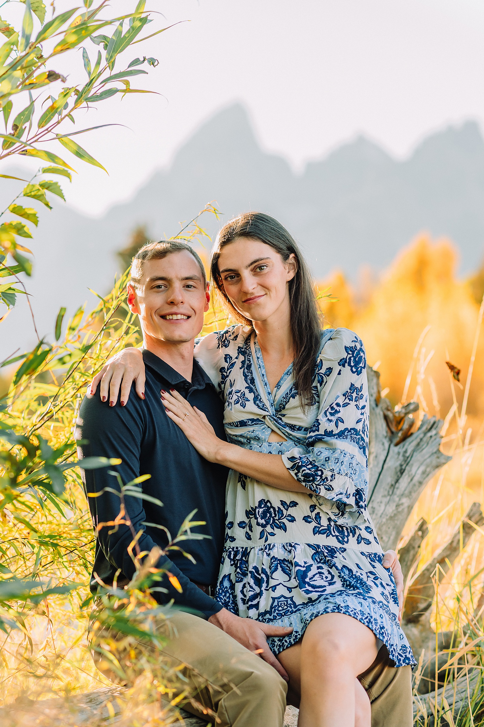 Jackson Hole engagement photos at Schwabacher Landing fall colors couple portraits along Snake River Wyoming autumn surprise engagement session Grand Teton National Park western hats engagement photos Jackson Wyoming fall engagement photos sagebrush Tetons backdrop blue dress engagement photos Jackson Hole Wyoming Schwabacher Landing couples photography fall season golden cottonwood trees engagement portraits Wyoming