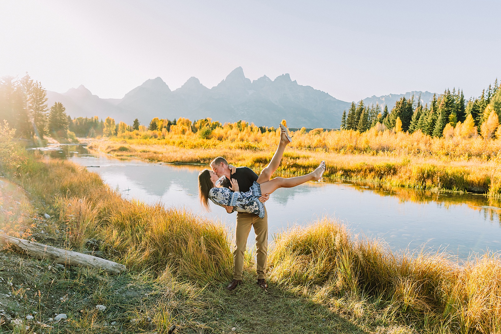 Jackson Hole engagement photos at Schwabacher Landing fall colors couple portraits along Snake River Wyoming autumn surprise engagement session Grand Teton National Park western hats engagement photos Jackson Wyoming fall engagement photos sagebrush Tetons backdrop blue dress engagement photos Jackson Hole Wyoming Schwabacher Landing couples photography fall season golden cottonwood trees engagement portraits Wyoming