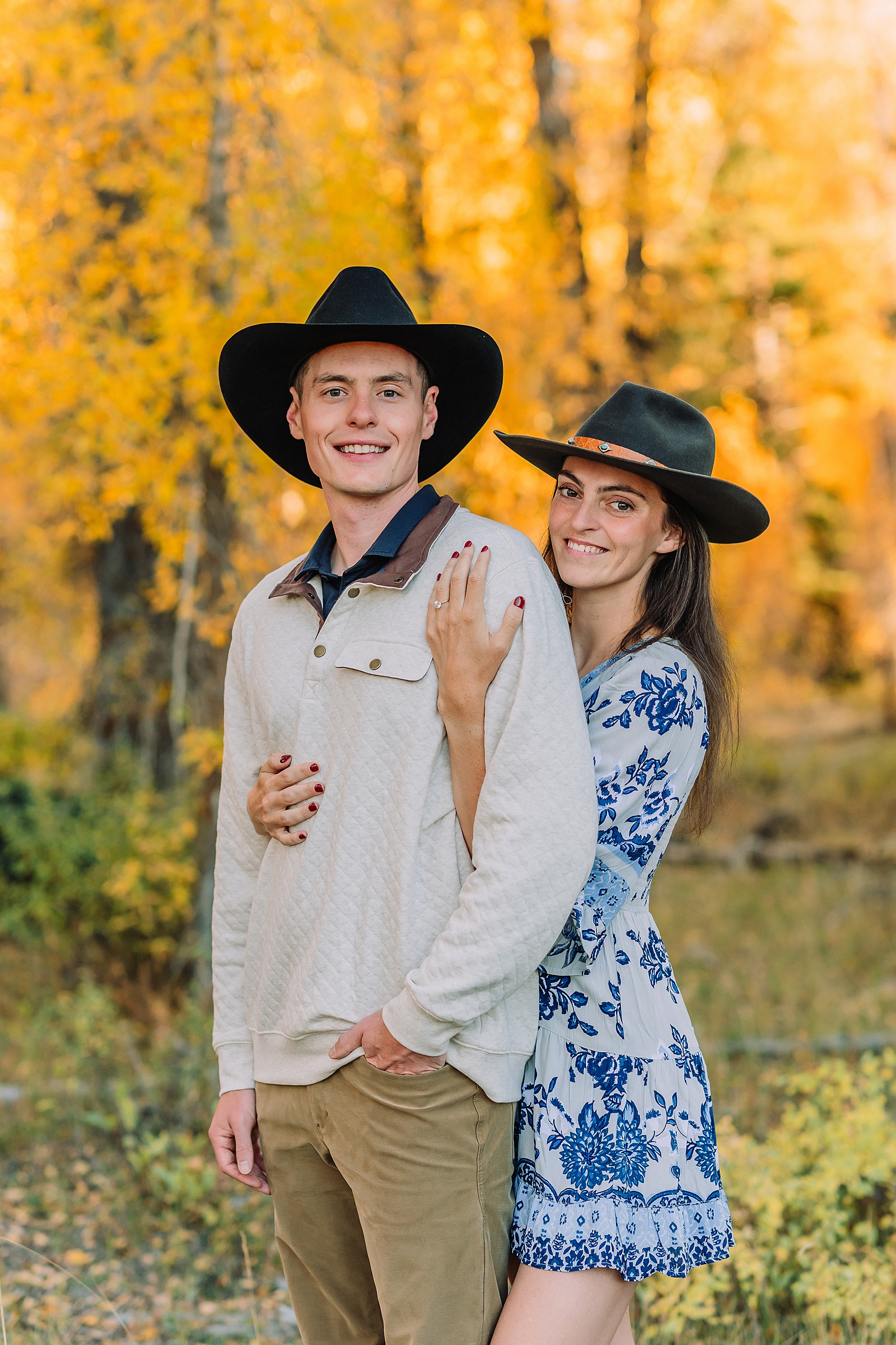 Jackson Hole engagement photos at Schwabacher Landing fall colors couple portraits along Snake River Wyoming autumn surprise engagement session Grand Teton National Park western hats engagement photos Jackson Wyoming fall engagement photos sagebrush Tetons backdrop blue dress engagement photos Jackson Hole Wyoming Schwabacher Landing couples photography fall season golden cottonwood trees engagement portraits Wyoming