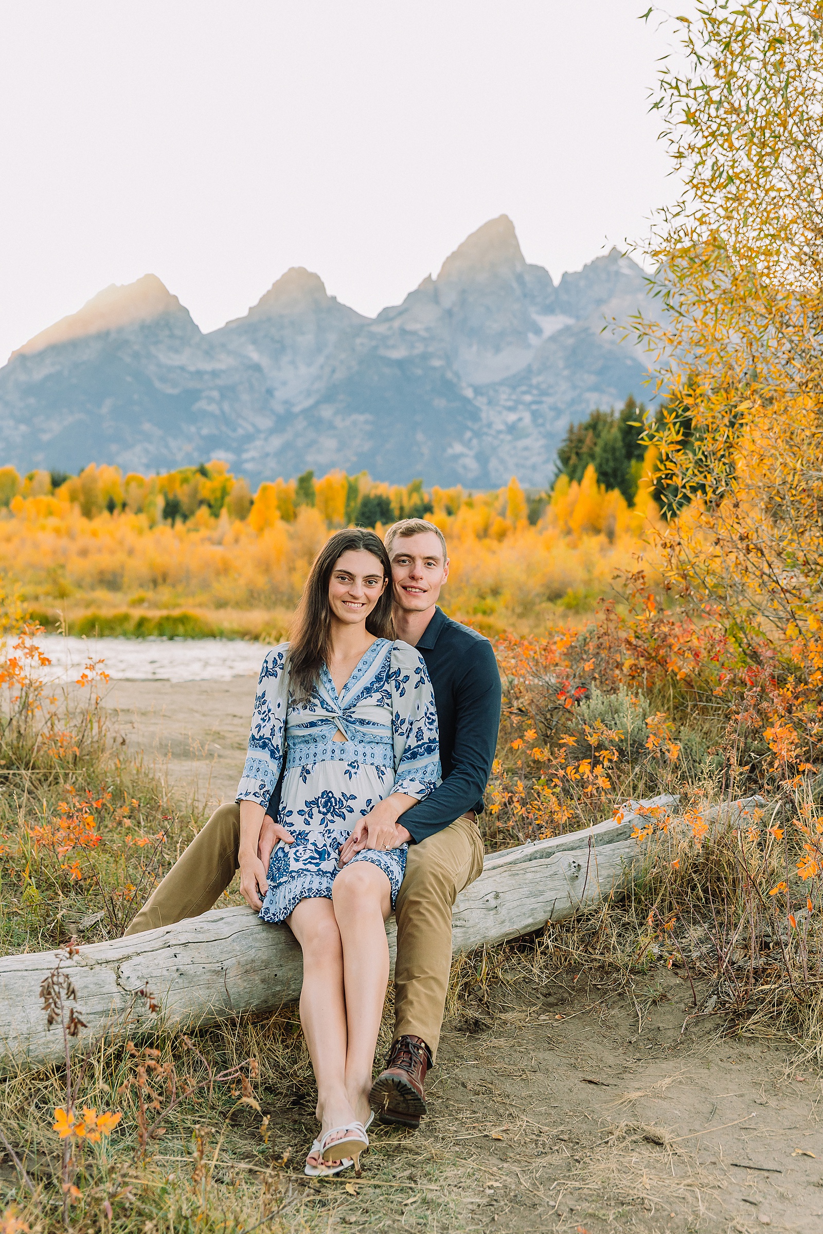 Jackson Hole engagement photos at Schwabacher Landing fall colors couple portraits along Snake River Wyoming autumn surprise engagement session Grand Teton National Park western hats engagement photos Jackson Wyoming fall engagement photos sagebrush Tetons backdrop blue dress engagement photos Jackson Hole Wyoming Schwabacher Landing couples photography fall season golden cottonwood trees engagement portraits Wyoming