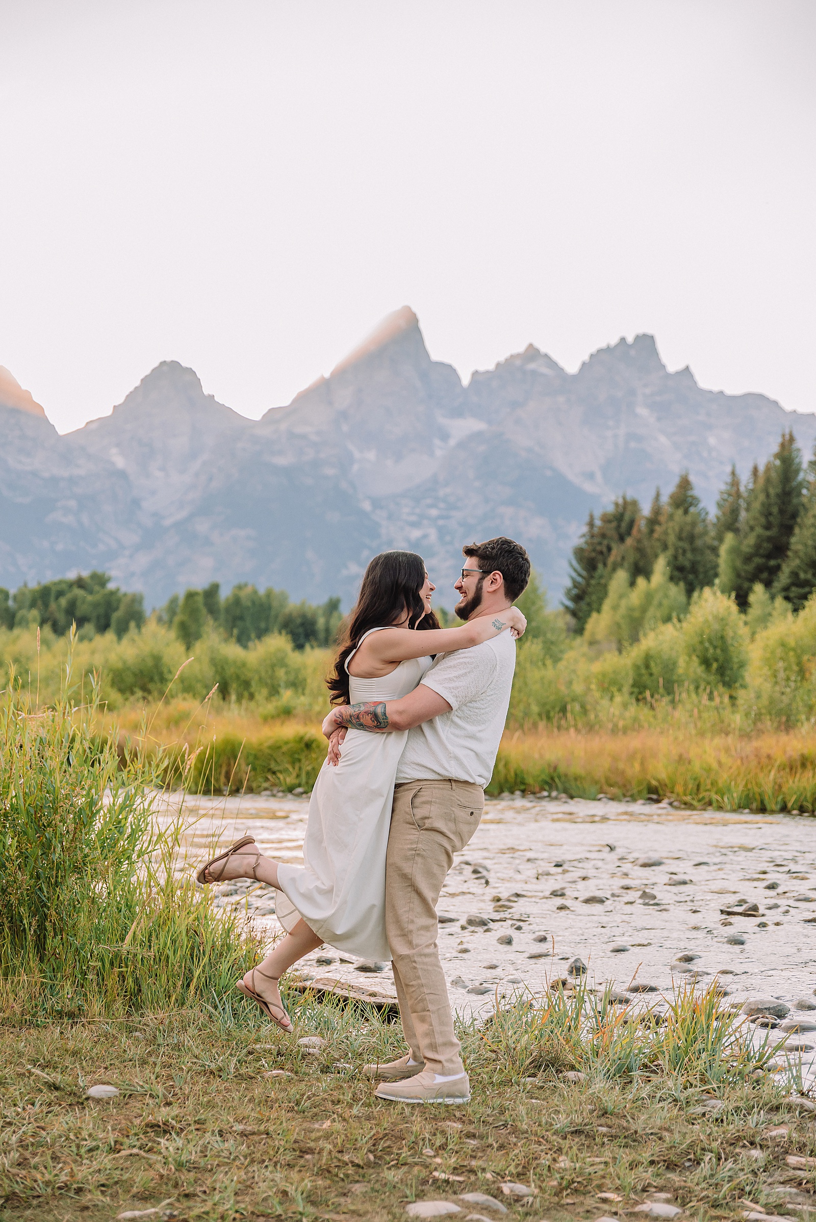Schwabacher Landing engagement photos Grand Teton National Park white corset dress mountain engagement session Wyoming sunset engagement photos Teton mountain range backdrop couple wearing white outfits Grand Teton engagement shoot Jackson Hole Engagement Photographer
