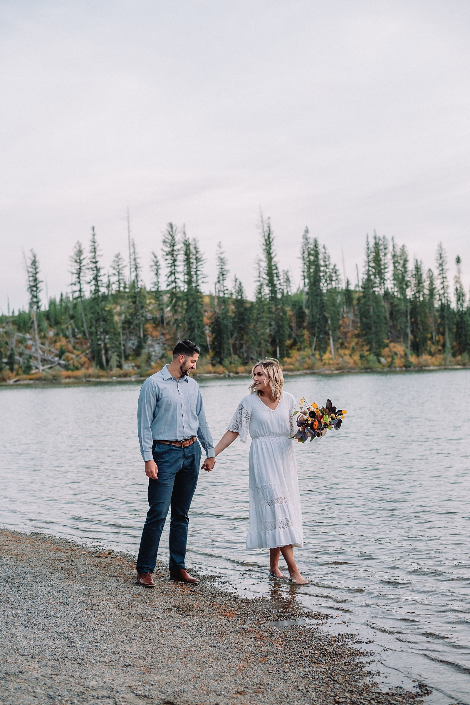 bride and groom walking in lake teton mountains beach