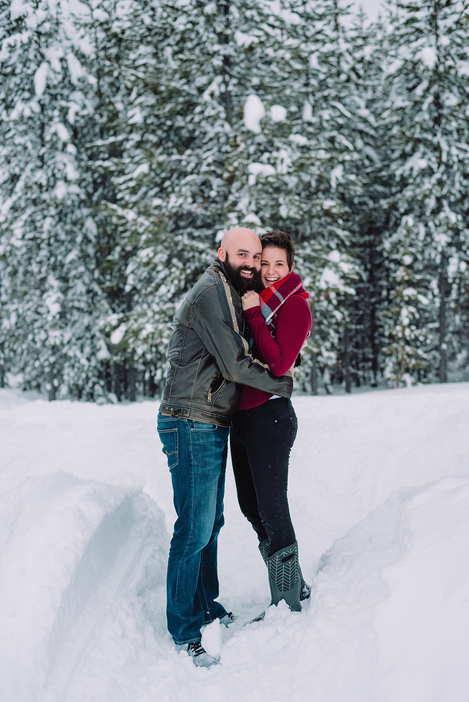 couple in front of flocked pine trees snow winter engagements