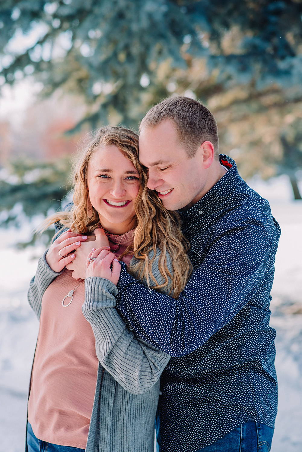 janelle and co photography engaged couple walking and laughing in the snow winter photos wedding photographer idaho falls freeman park engagement photos in the pine trees forest romantic and traditional