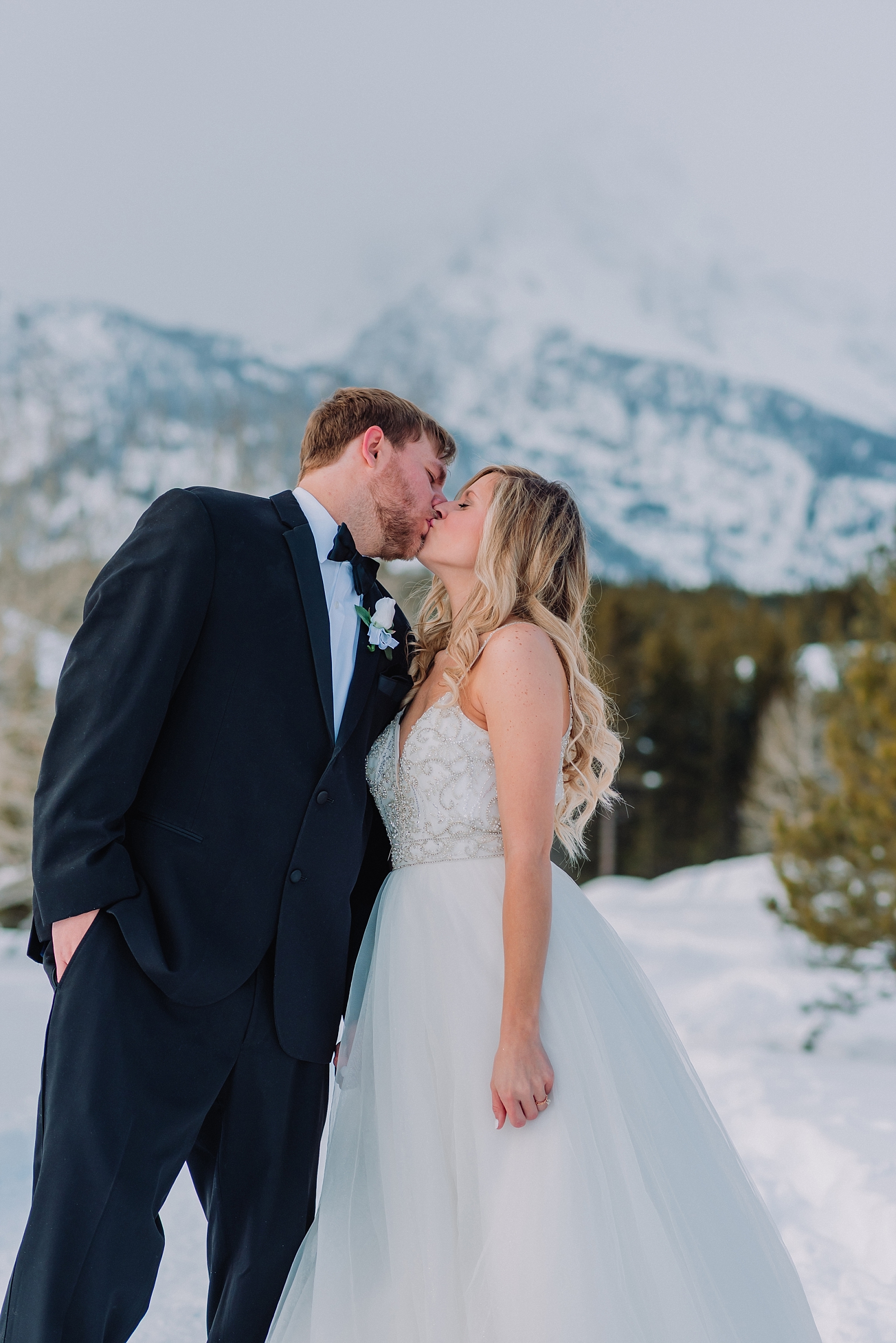 groom kissing bride while standing in snow under the teton mountains in grand teton national park gtnp winter in JH wedding photographer