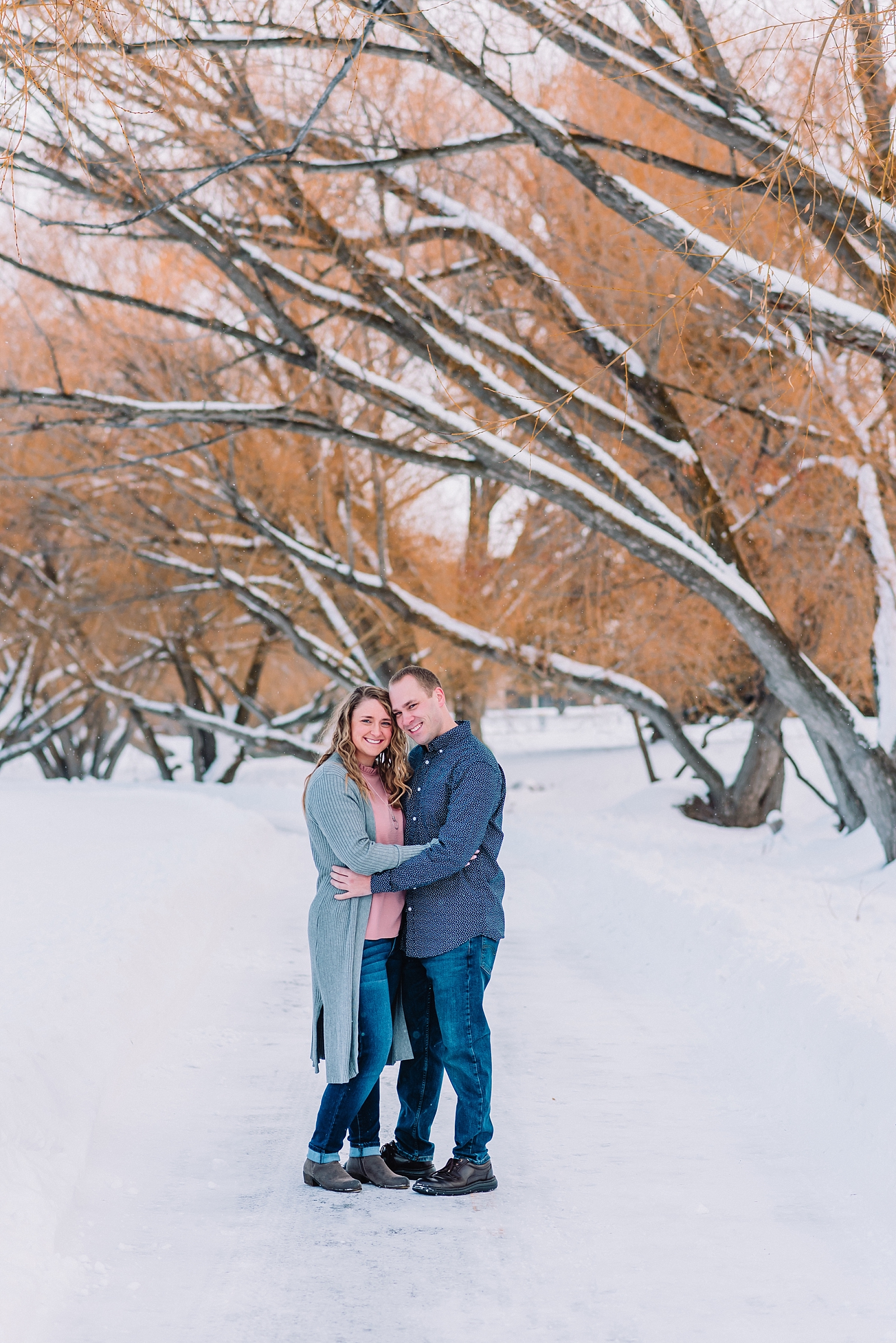 engaged couple standing on snowy bank