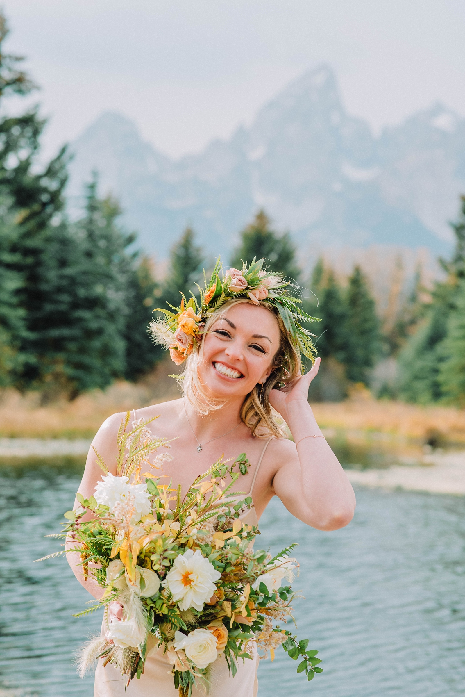 bride holding her warm neutral wedding bouwuet in the Grand Tetons in front of a lake