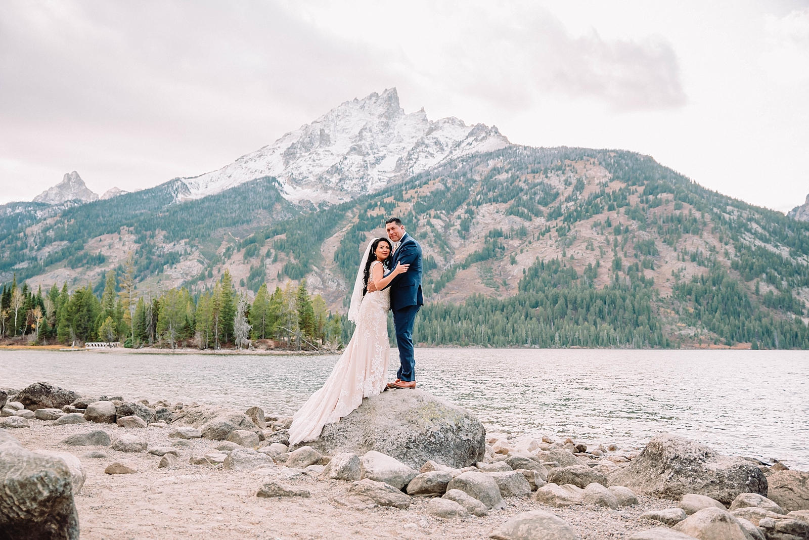 bride and groom standing on a rock at a lake int he Grand Tetons