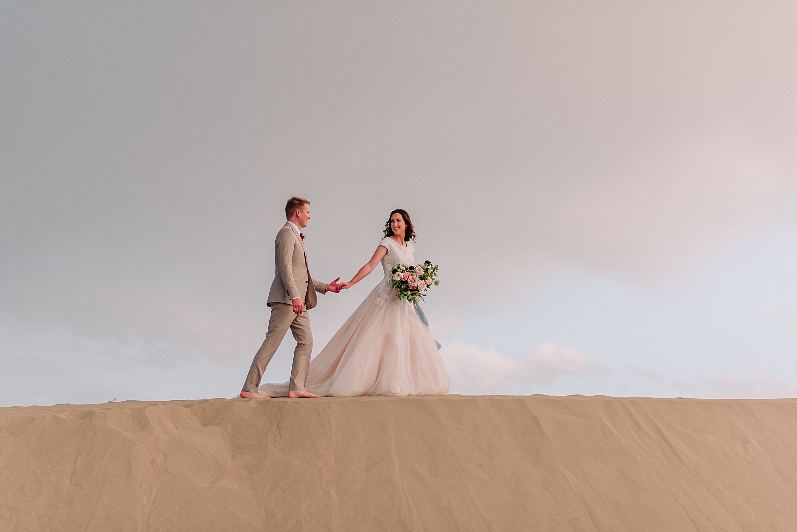 bride and groom walking in sand dunes celebrating wedding