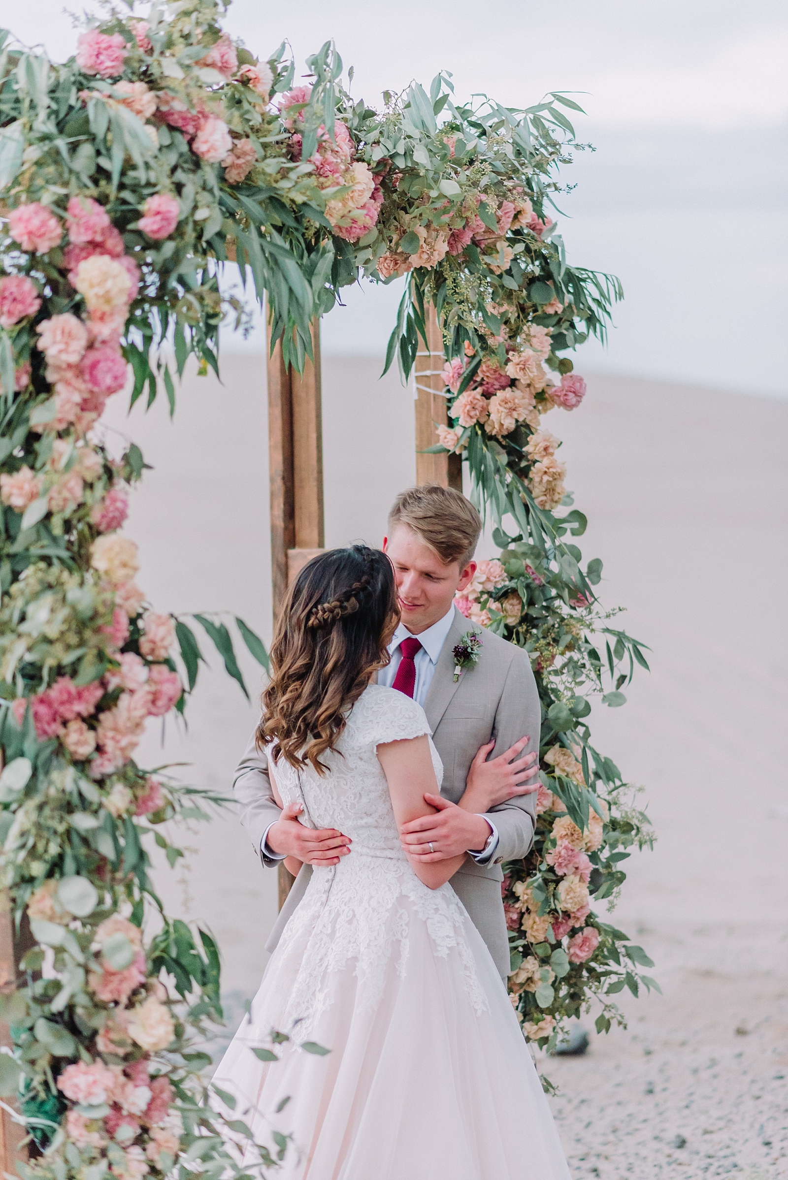 bride and groom embrace each other while standing under a beautiful wedding arch covered in florals