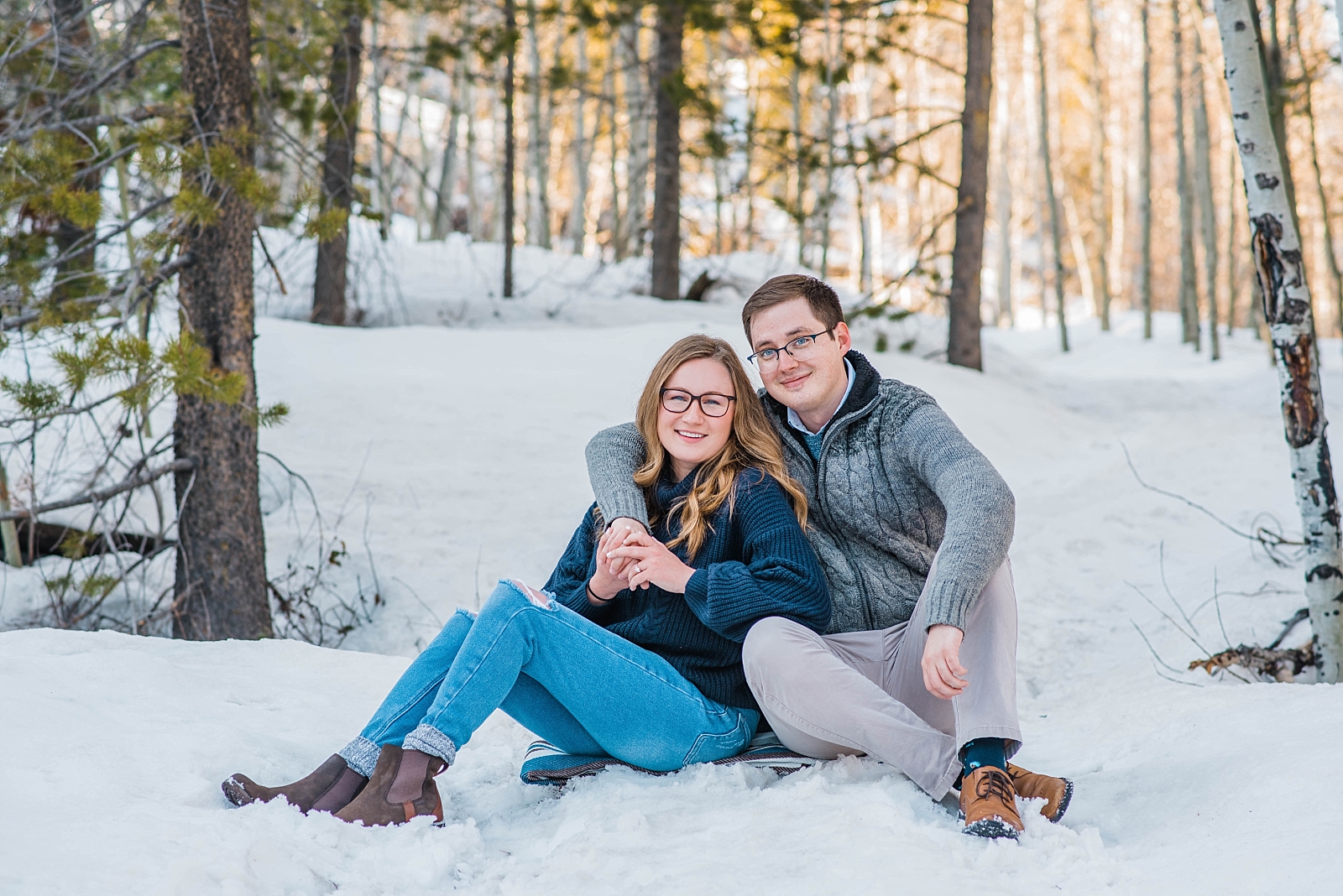 couple sitting on snowy ground during outdoor engagements at taggart lake