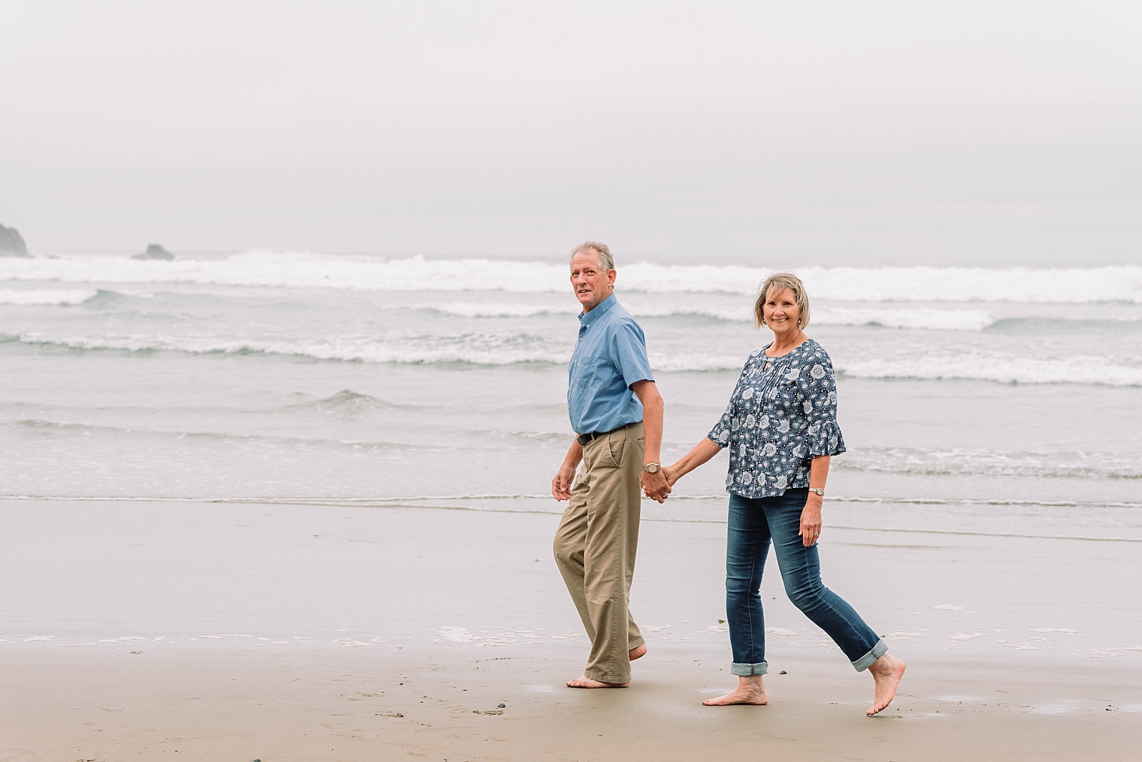 couple walks on the beach while holding hands at the oregon coast
