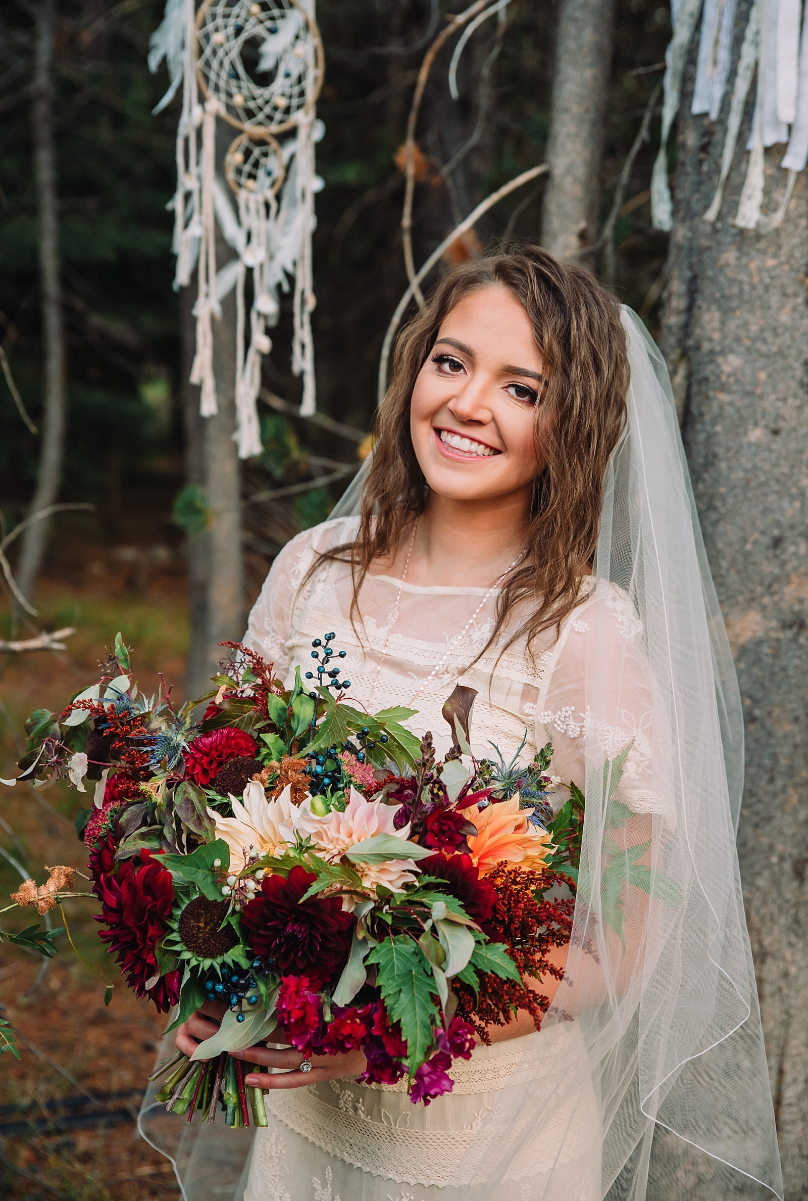 boho bride in Jackson hold Idaho elopeing into the woods holds a beautiful red bouquet while wearing a vintage wedding dress