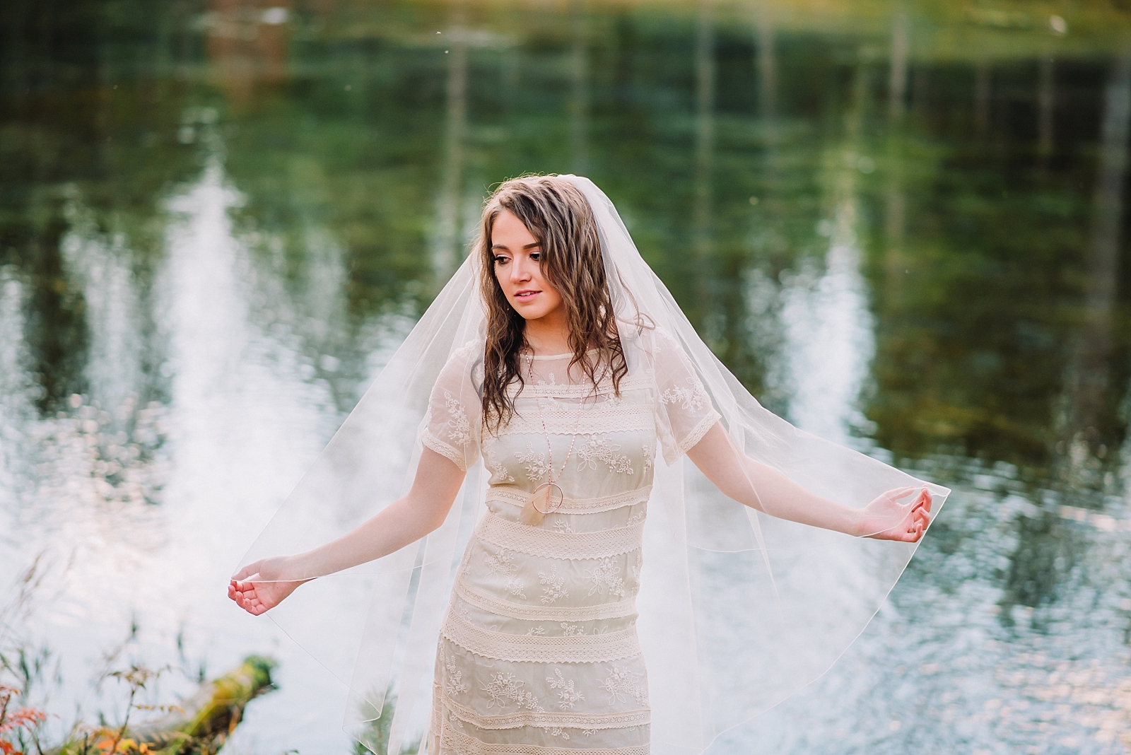 bride in a lace vintage dress and long veil standing infront of an Island Park Lake in Idaho holding out her veil 