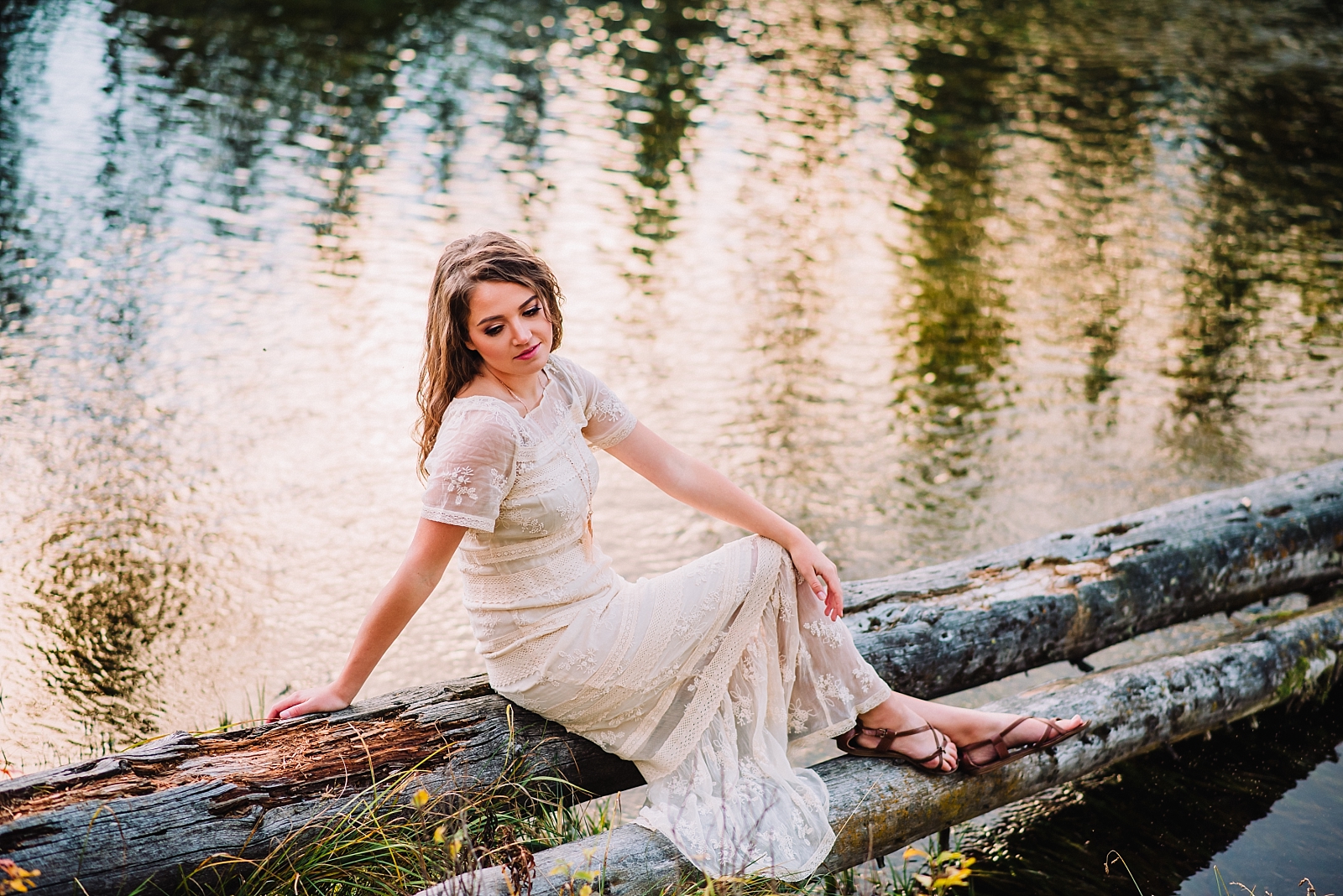 bride on her wedding day sitting on a log in Island Park in front of a lake