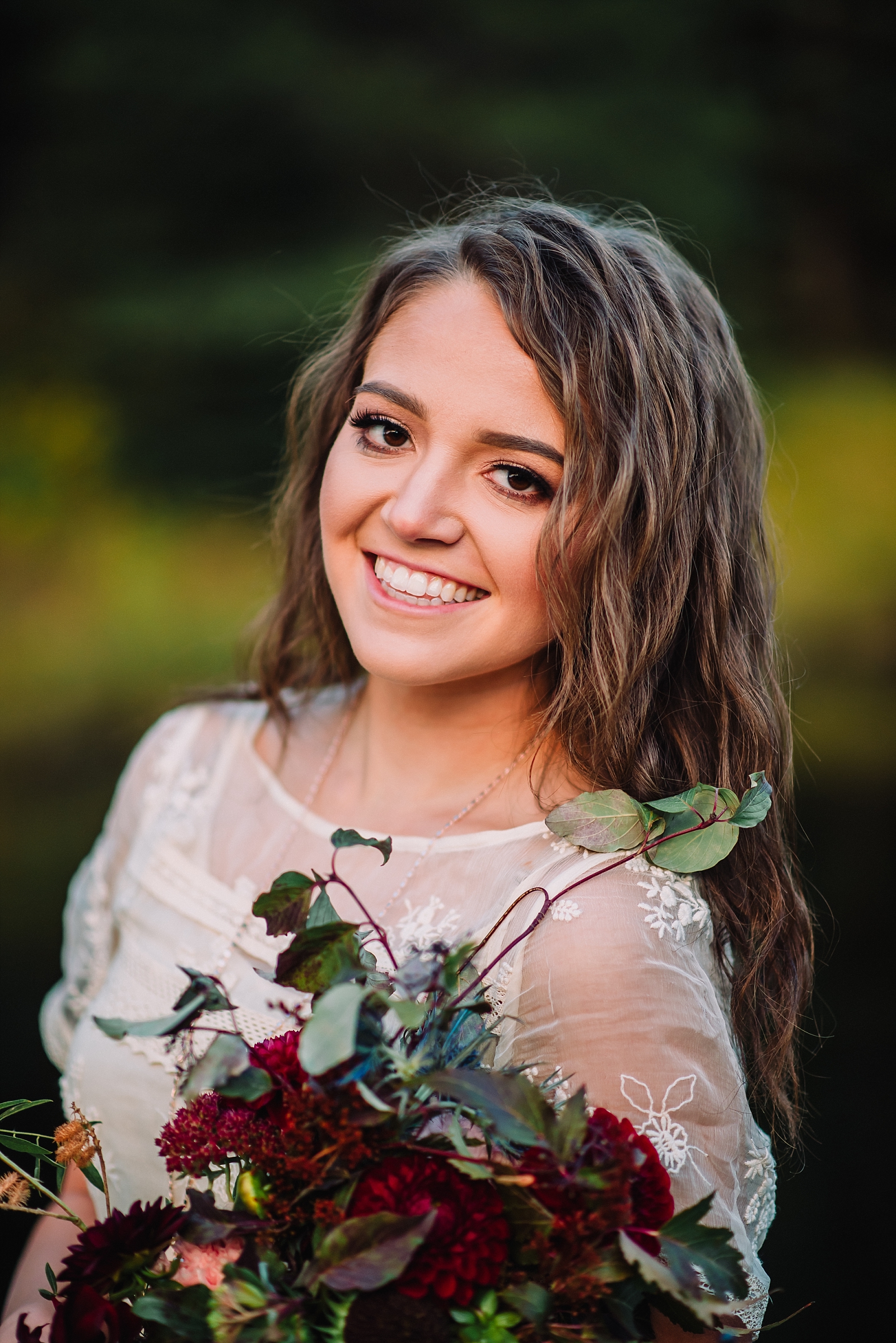 bride smiling at the camera while holding a burgundy bridal bouquet wearing a lace dress