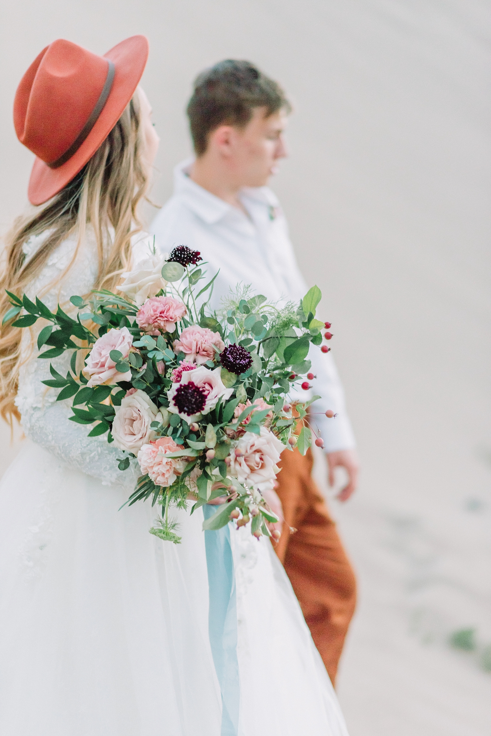 neutral pink floral bouquet held by boho bride with a red hat on