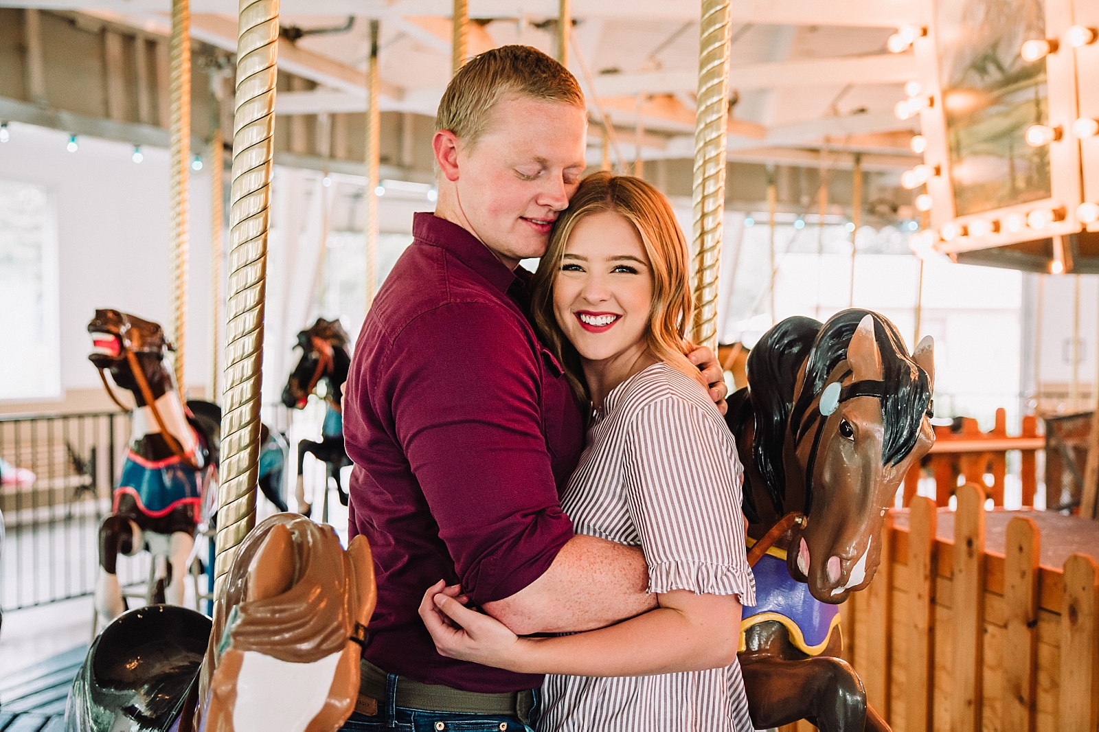 young couple hugging while woman smiles at camera on rexburg carousel