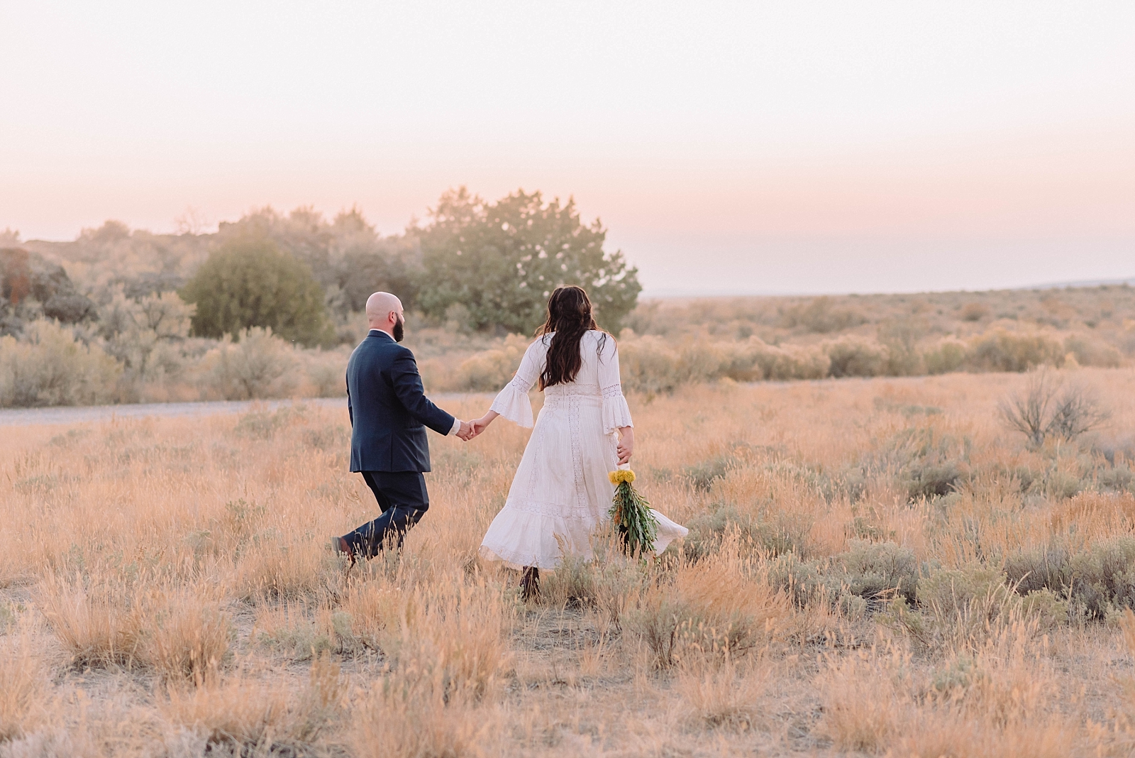 bride and groom walking hand in hand in field after elopement at hell's half acre