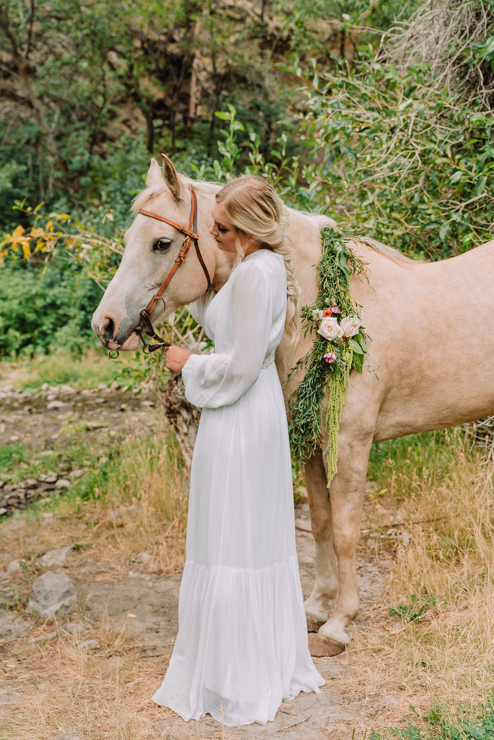 bride tending to horse in styled elopement wearing long sleeve boho chic gown