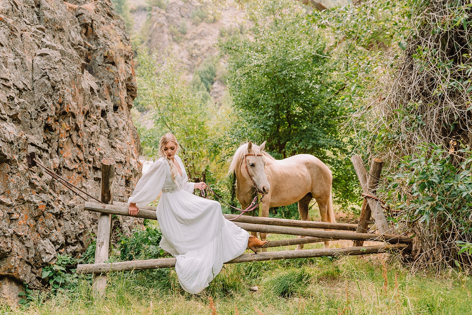 bride sitting on rustic fence wearing boho chic inspired gown with horse