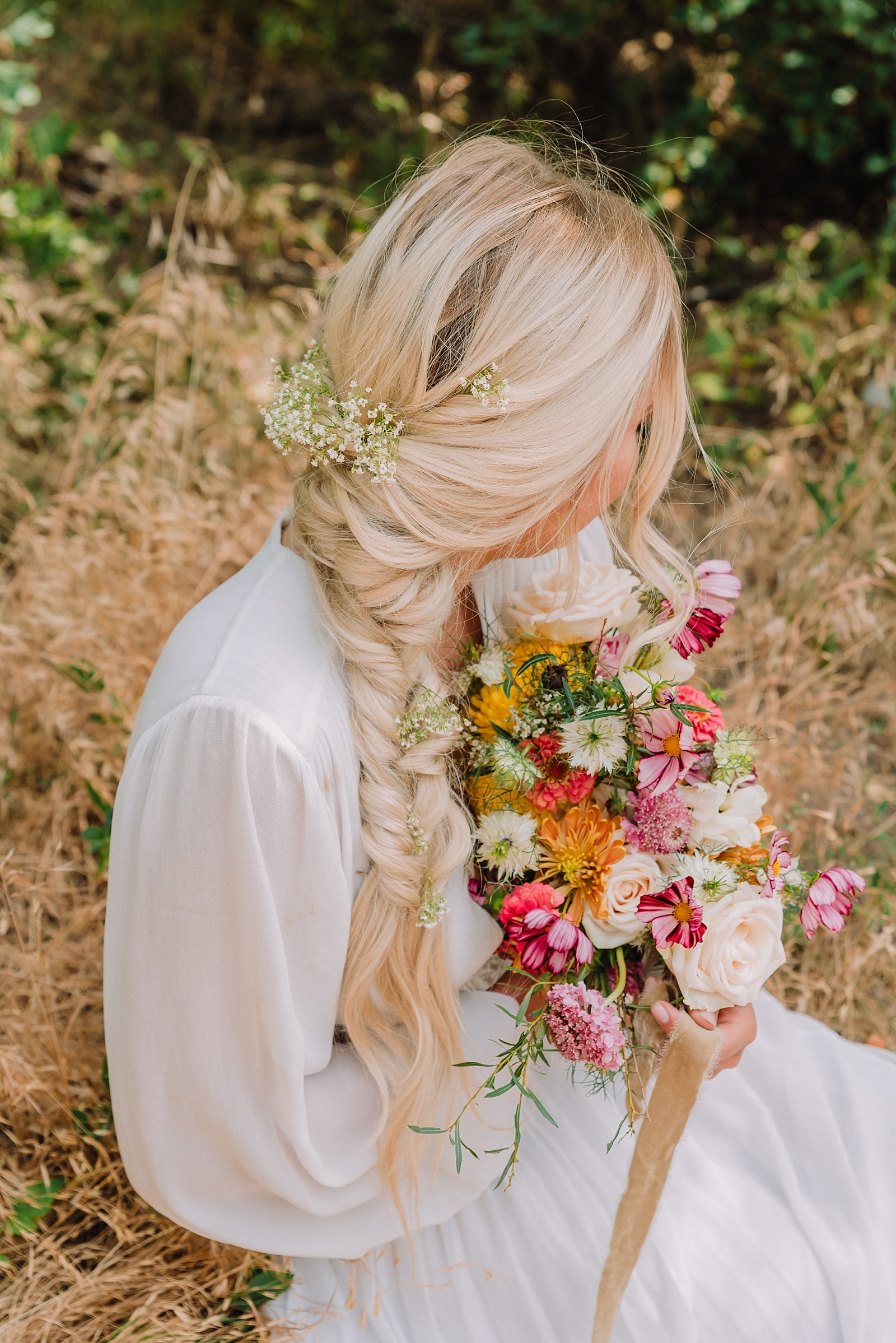 bride sitting in boho chic long sleeve wedding gown holding colorful bouquet with braided hair