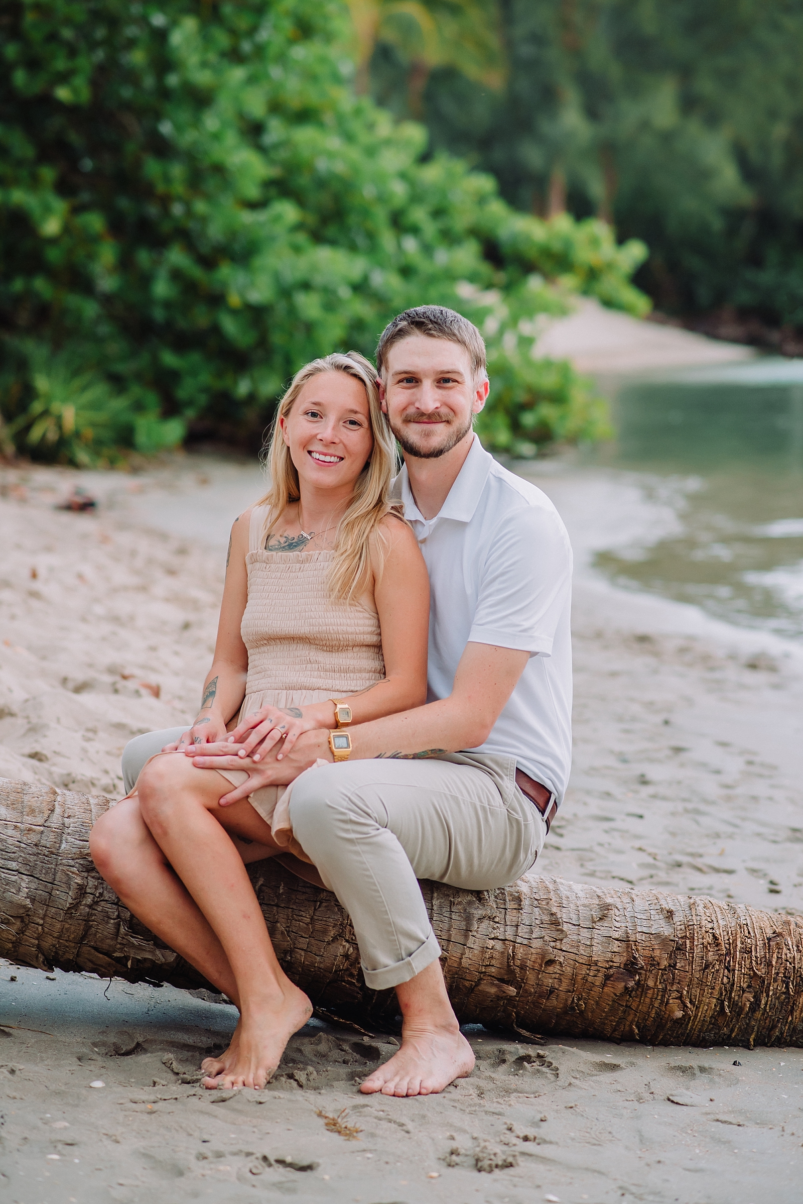 engaged couple sits on log on beach