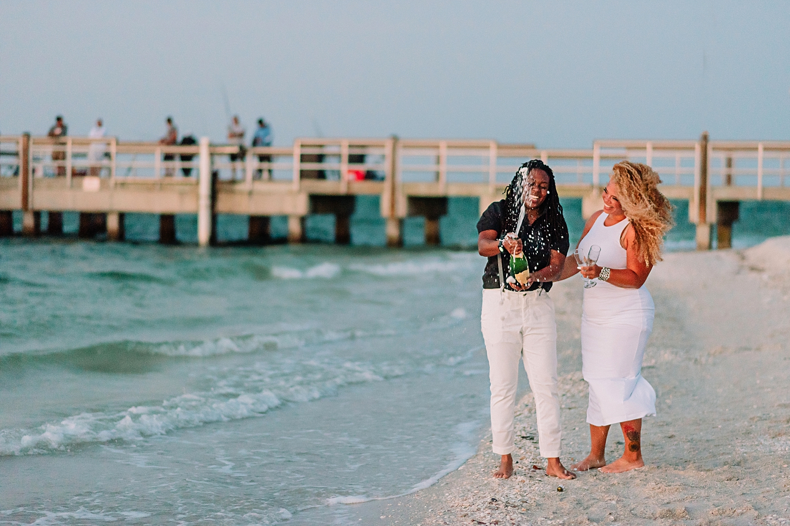 Lesbian engagements on Sanibel Island. Same-sex couple celebrates with champagne toasts on the beach in Florida.