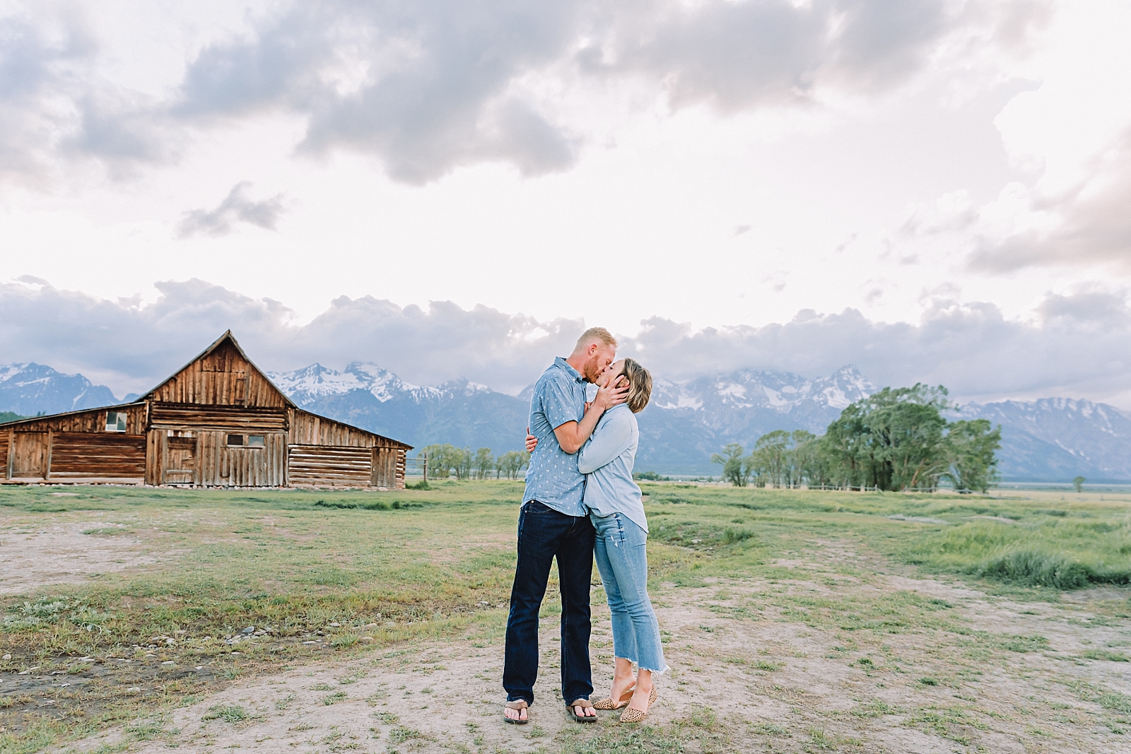 couple kisses in front of mormon row barn