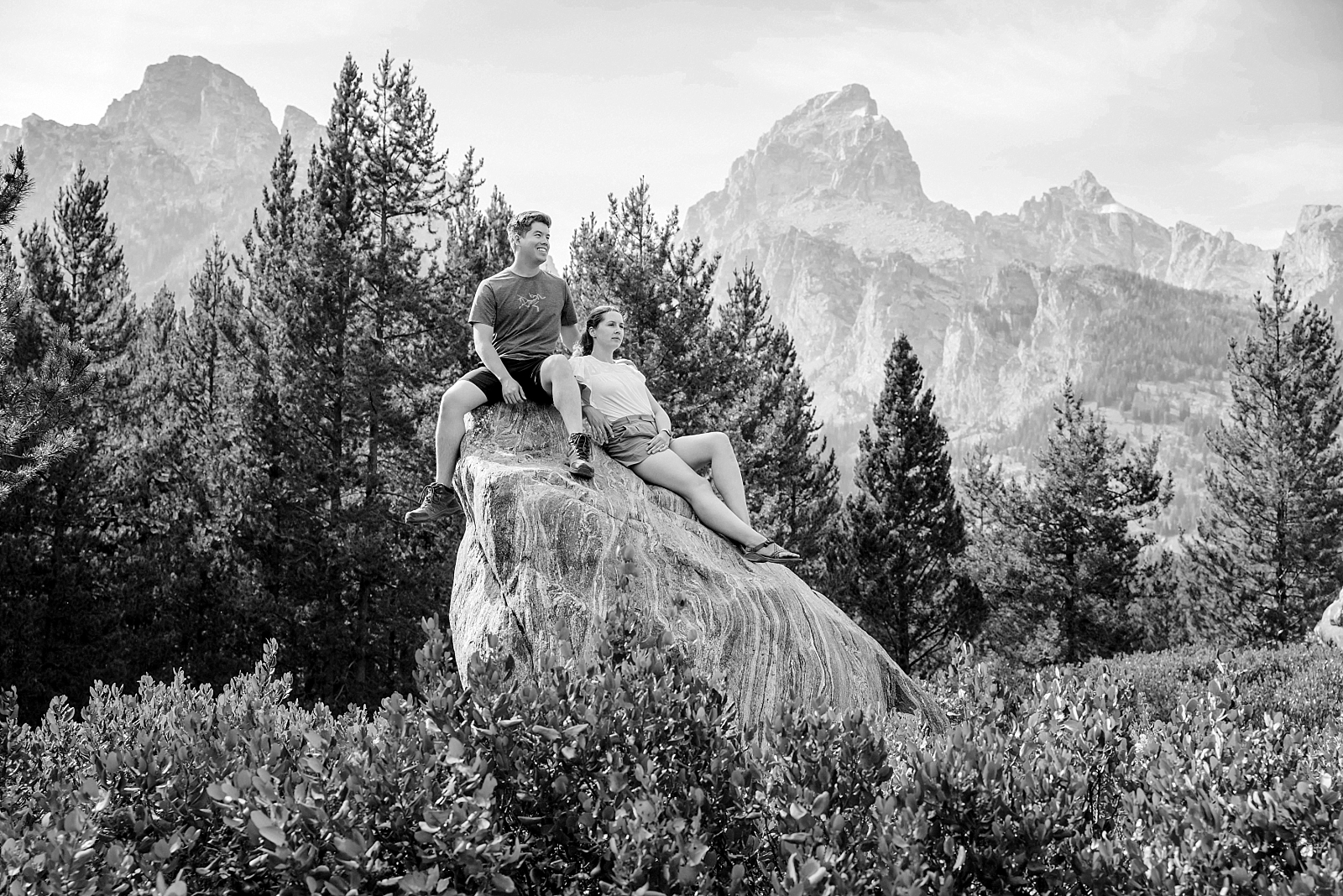 engaged couple climbs on rocks in the tetons