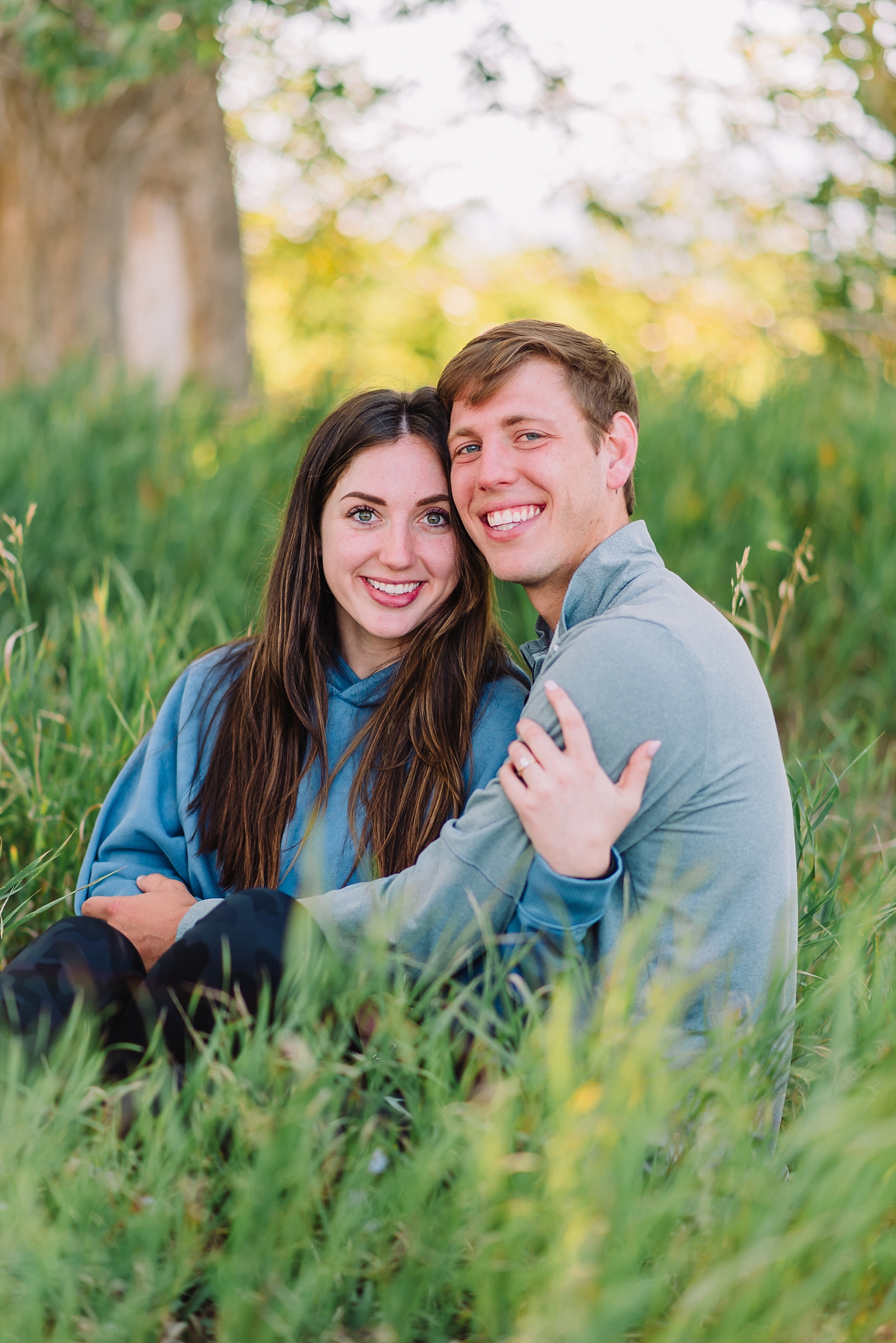 engaged couple sits in grass