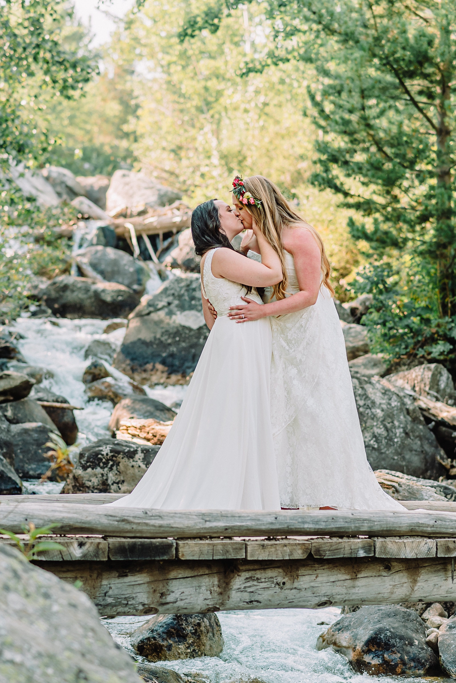 two brides kiss on bridge with waterfall in lesbian wedding