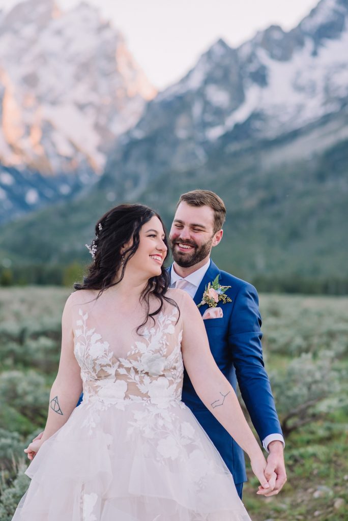 groom standing behind his bride and holding her hands as she looks over her shoulder on their wedding day in Grand Teton National Park