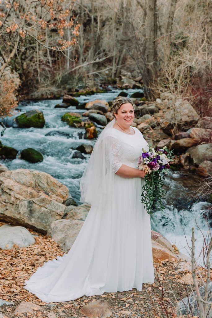 Idaho bride standing on rocks next to a waterfall as she holds her Spring florals